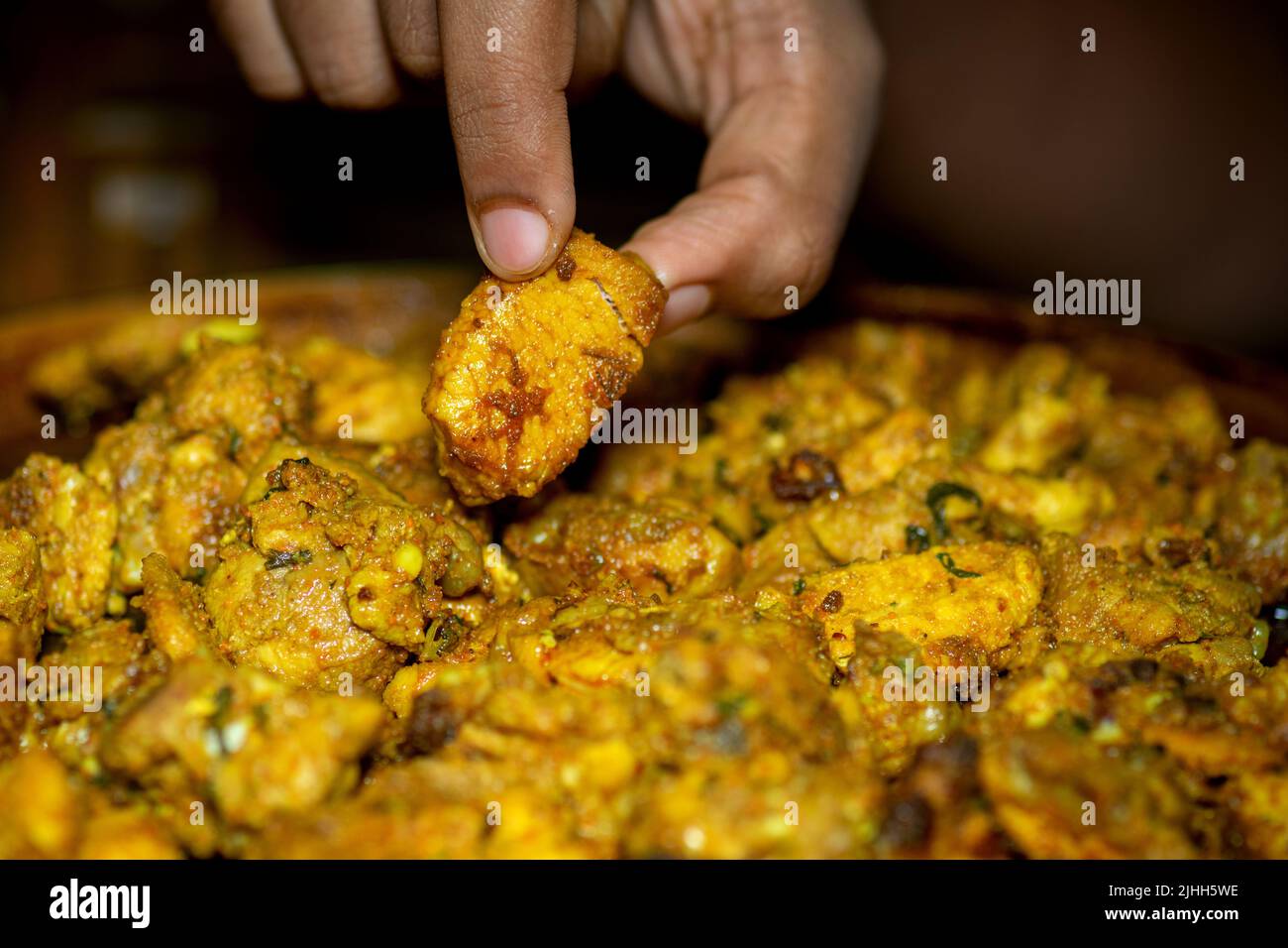 Würzige Hähnchenstücke auf der Pfanne und eine in den Fingern für die Überprüfung während des Rezepts von Butter Huhn nach dem Entfernen von Wasser aus Stücken gepflückt. Selektiver Fokus verwendet Stockfoto