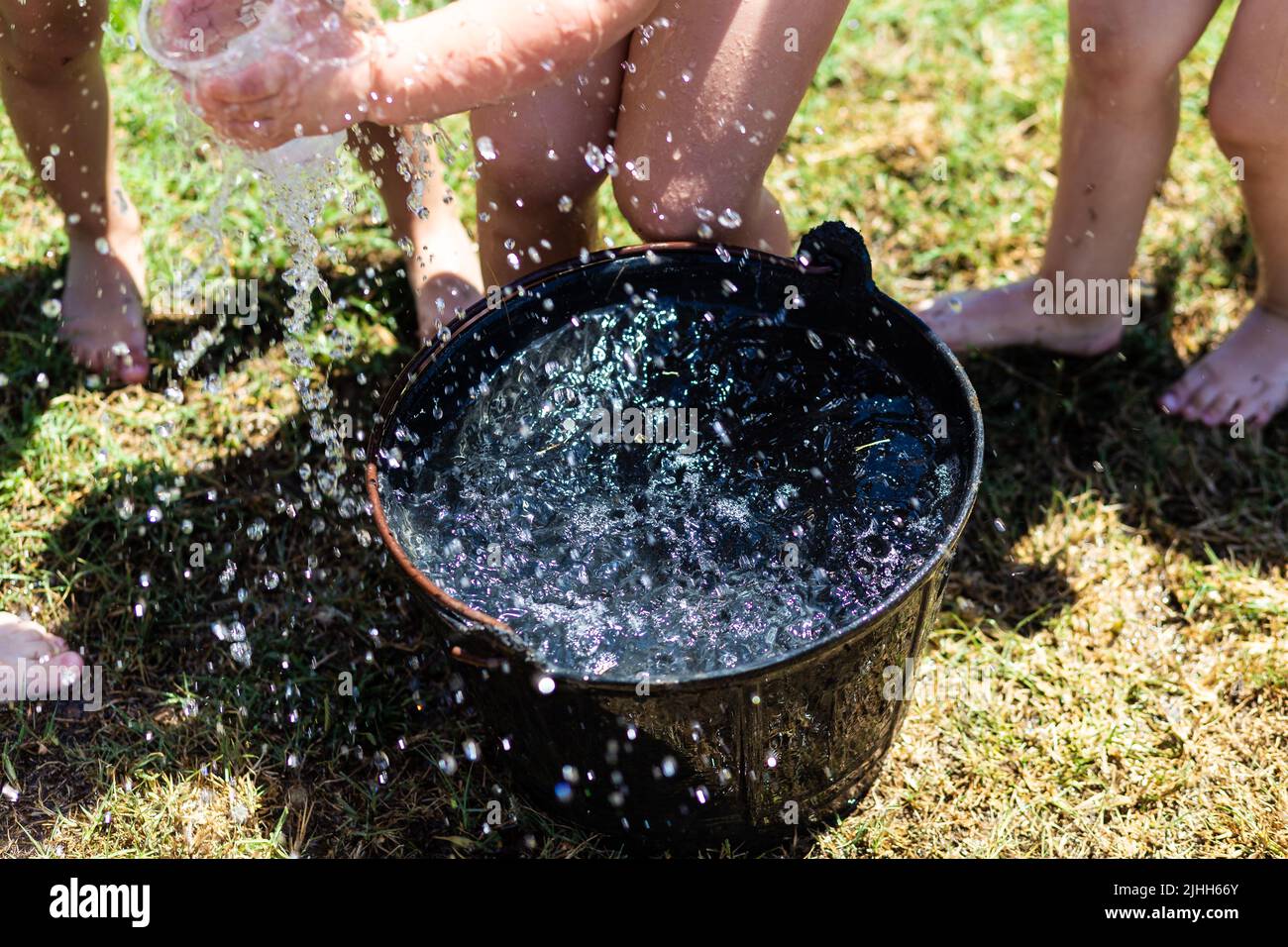 Schwarzer Plastikeimer mit frischem Wasser mit vielen Beinen für Kinder, die Sommerspiele auf einer grünen Wiese spielen Stockfoto