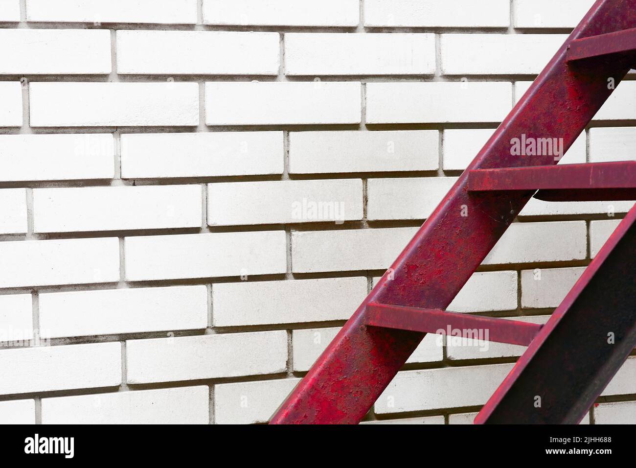 Ein Teil der Treppe führt durch eine rote Metallleiter, die gegen eine weiße Ziegelwand führt Stockfoto