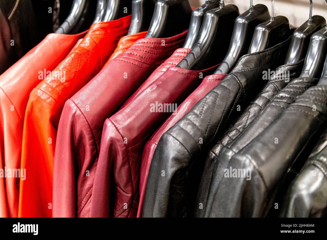 Bunte Lederjacken in Rot und Schwarz hängen an einer Schiene Stockfoto