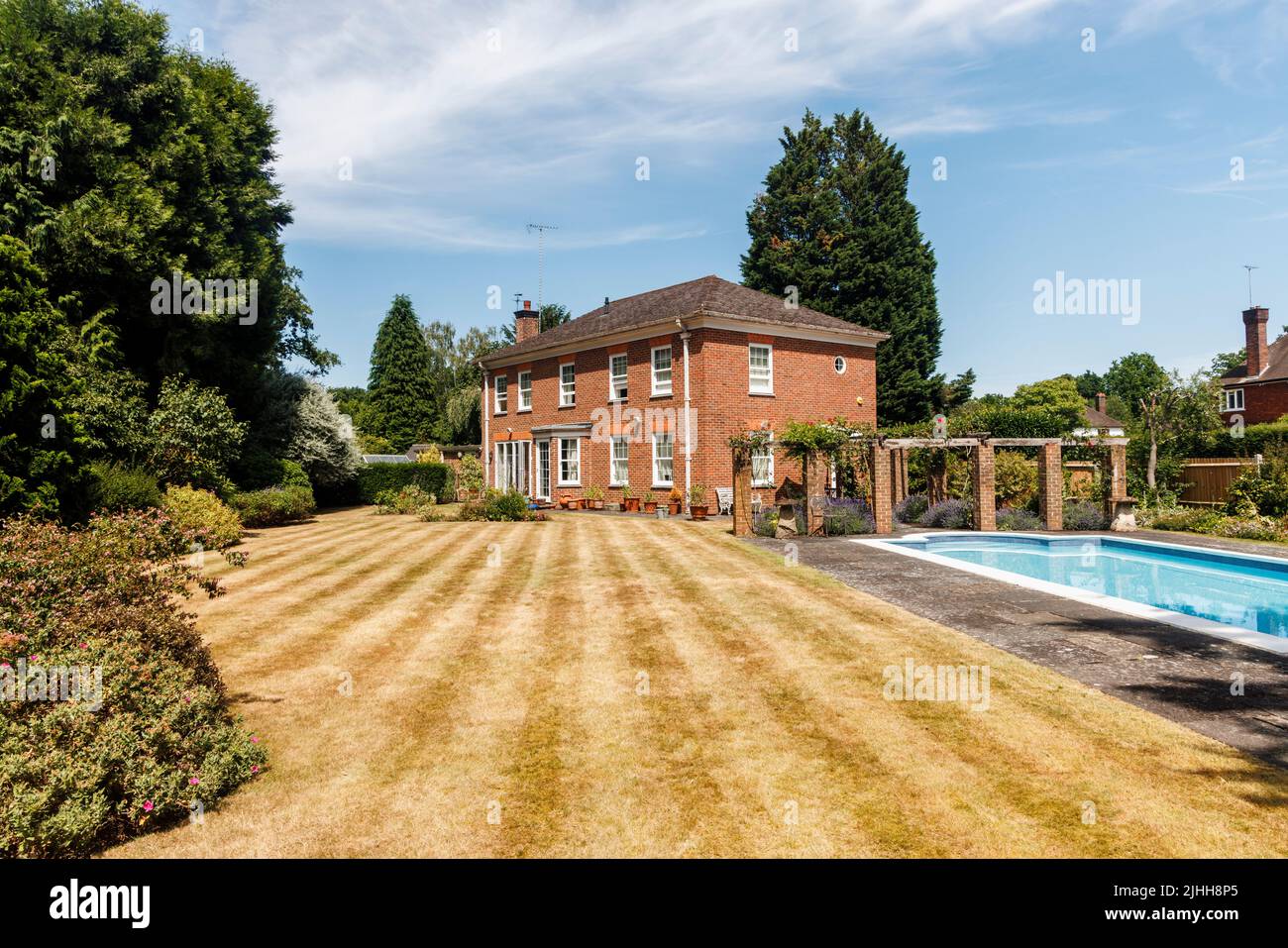 Außenansicht eines Einfamilienhauses, Garten und Schwimmbad, der Rasen mit Streifen, aber braun von Trockenheit und heißen Temperaturen im Sommer, Surrey, Großbritannien Stockfoto