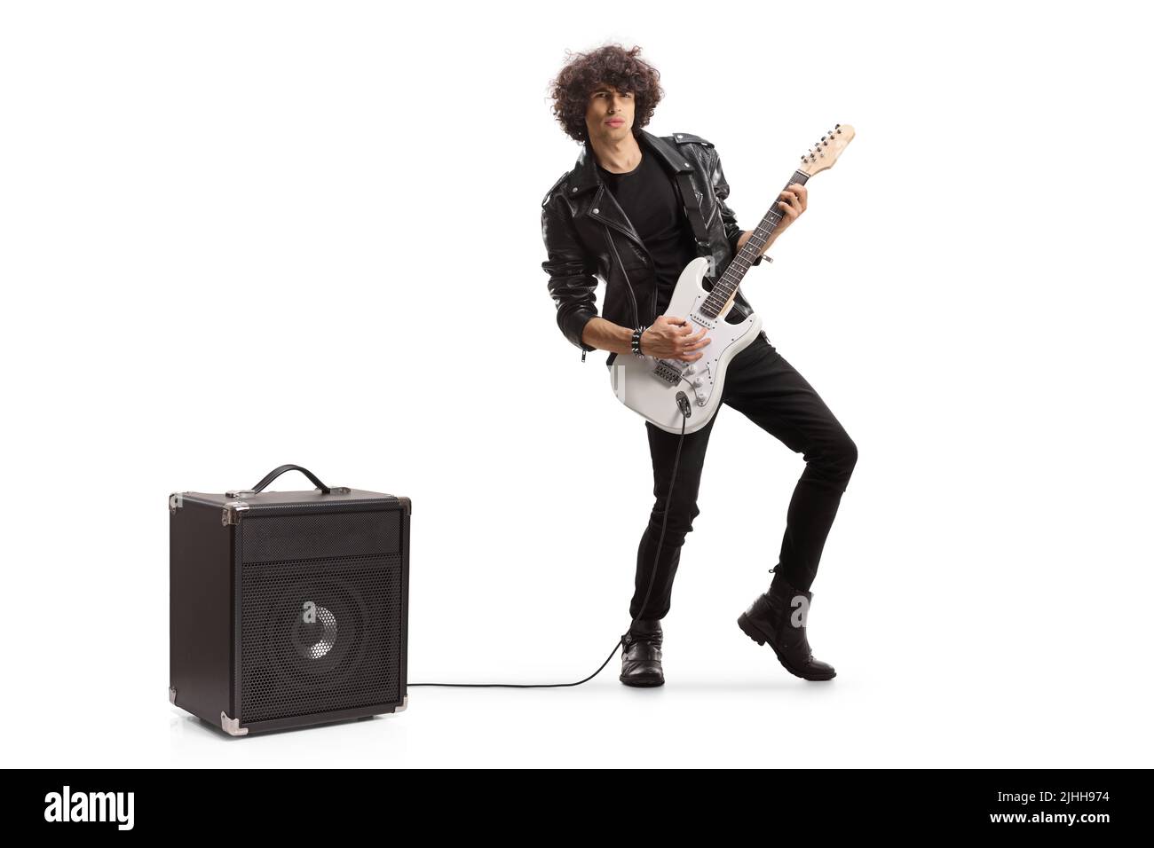 In voller Länge Porträt eines jungen Rockmusikers, der eine Gitarre spielt, die in einen auf weißem Hintergrund isolierten Verstärker eingesteckt ist Stockfoto