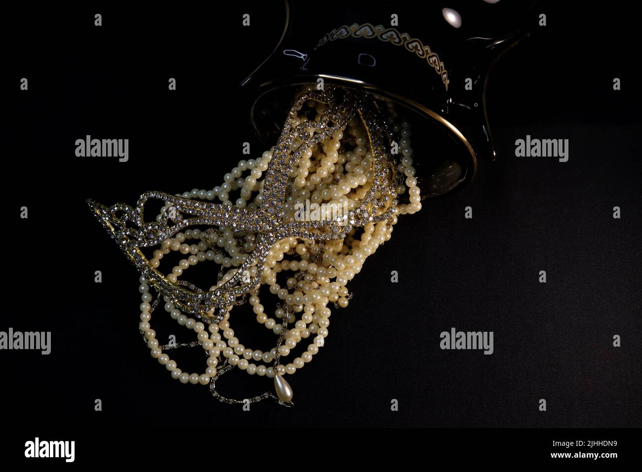 Ein Haufen verschiedener Perlenketten aus nächster Nähe und auf neutralem Hintergrund mit Add-ons wie einer Vase, einem alten Hut, einer Maske und rot-goldenen Aufbewahrungsbehältern. Stockfoto