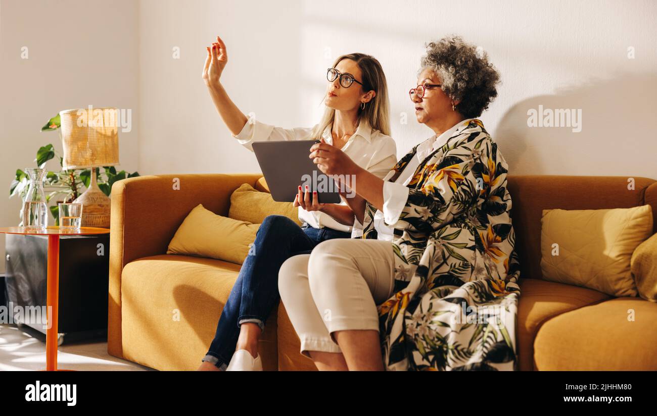 Innenarchitekten diskutieren eine neue Idee, während sie in der Lobby eines modernen Büros sitzen. Zwei Geschäftsfrauen, die zusammen mit einem digitalen Tablet arbeiten Stockfoto