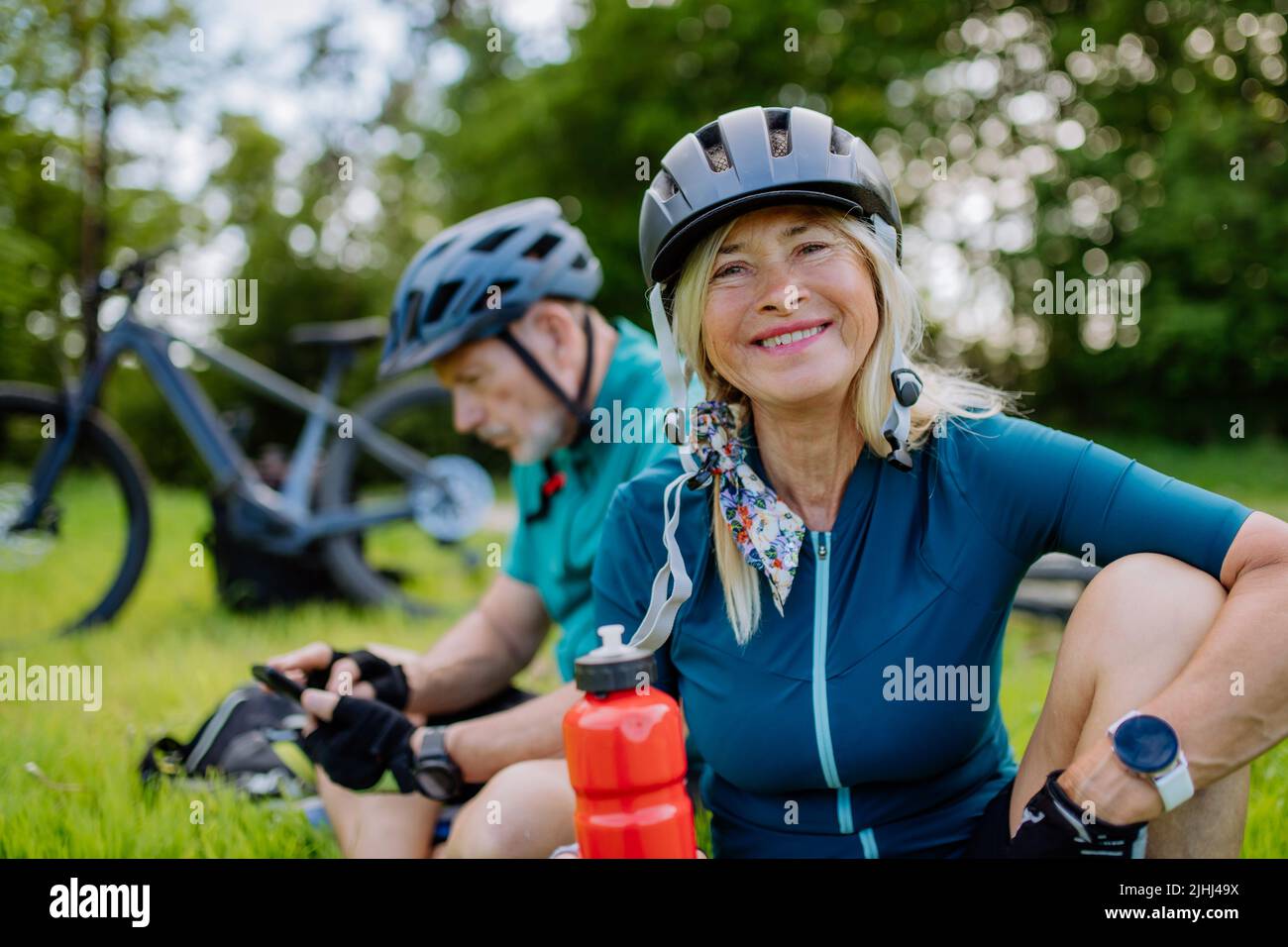 Aktives Seniorenpaar, das sich nach einer Fahrradtour im Sommerpark auf Gras und Trinkwasser ausruhte. Stockfoto