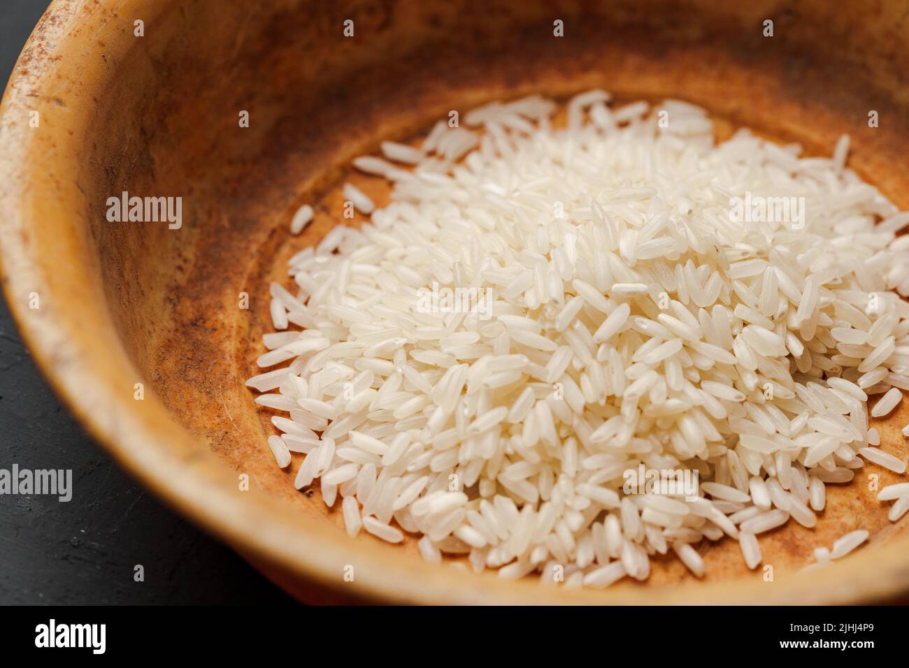 Haufen von trockenem Reis in einer Schüssel auf schwarzem Hintergrund, Mangel an Nahrung, Hunger-Konzept Stockfoto