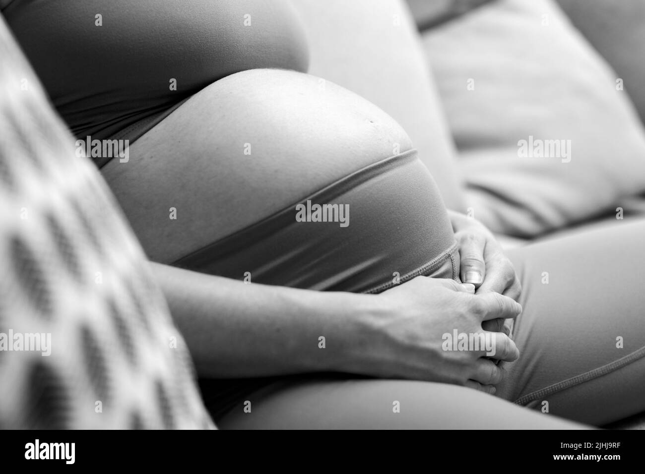 Bauch einer Schwangeren. Schwangerschaftskonzept. Schwanger Bauch Nahaufnahme. Detail der Schwangeren, die sich auf dem bequemen Sofa zu Hause in schwarz-weiß entspannen. Stockfoto