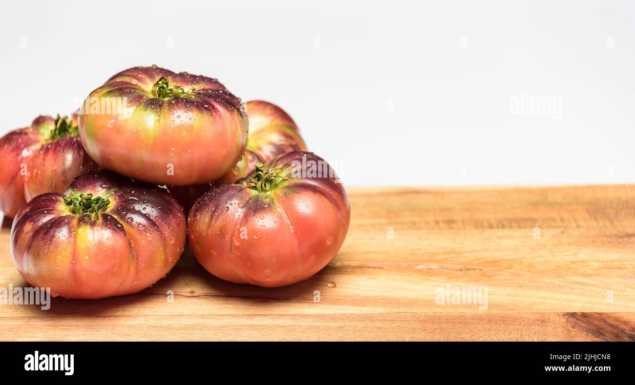 Tiger Tomate auf einem Schneidebrett mit Basilikumblättern auf Holzhintergrund. Speicherplatz kopieren. Frische Tomaten zum Kochen gejagt. Tomate mit Wassertropfen. Stockfoto