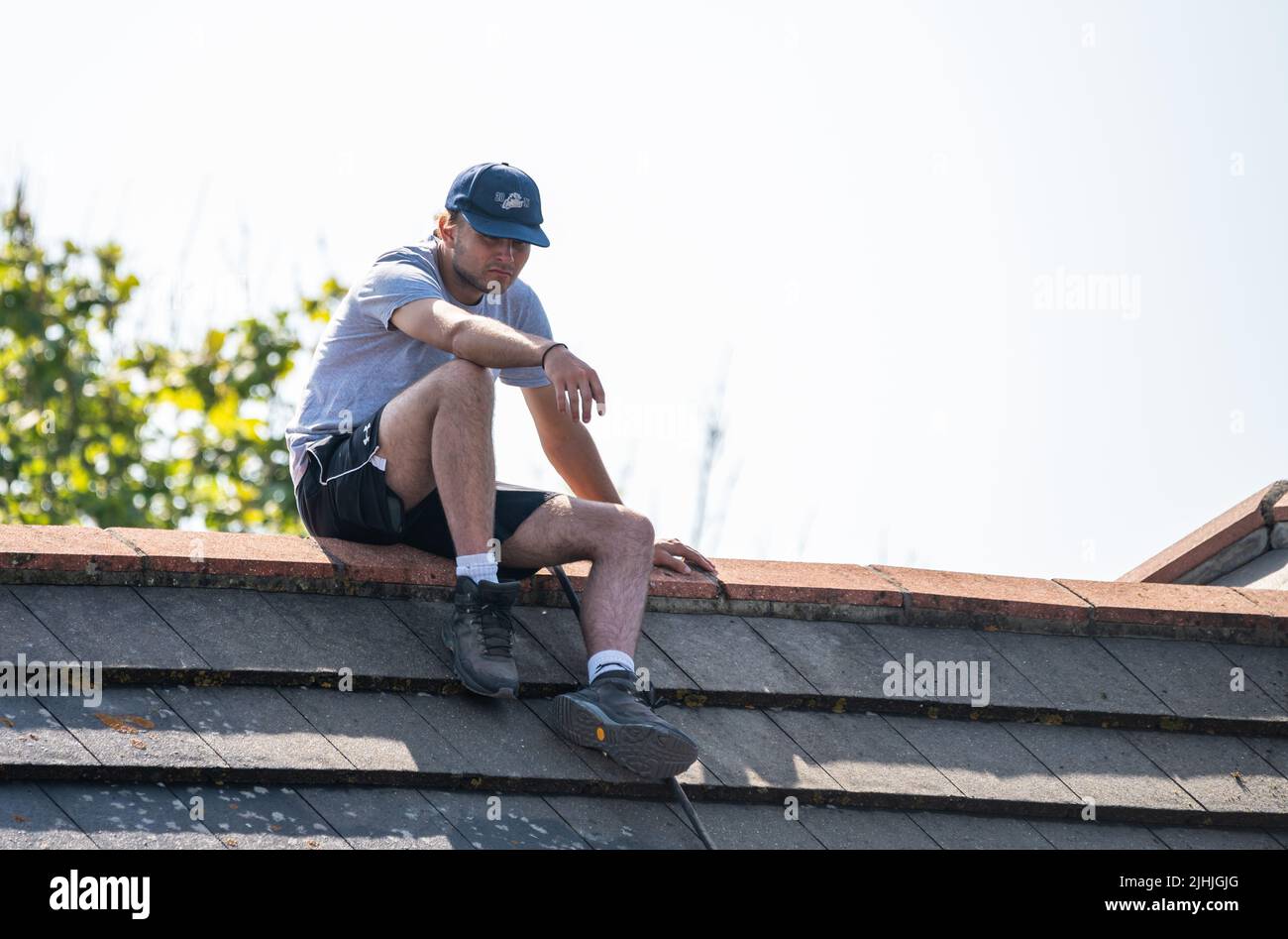 Rustington, West Sussex, Großbritannien. Dienstag, 19.. Juli 2022. Ein Mann sitzt heute Morgen in der sengenden Hitze auf einem Hausdach, während die Hitze in der Nähe der Südküste weiter anschwallen wird. Kredit: Geoff Smith/Alamy Live Nachrichten Stockfoto