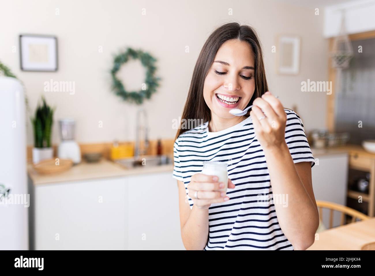 Heitere junge schöne Frau, die Bio-Joghurt in der Küche zu Hause isst Stockfoto