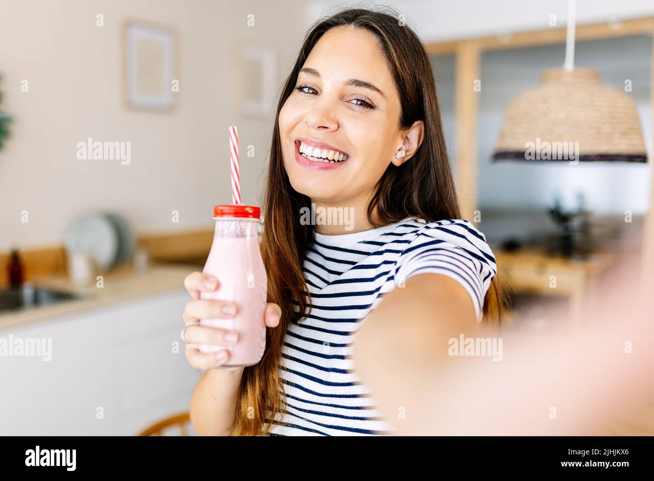Junge Frau mit Erdbeersaft nimmt Selfie in der Küche Stockfoto