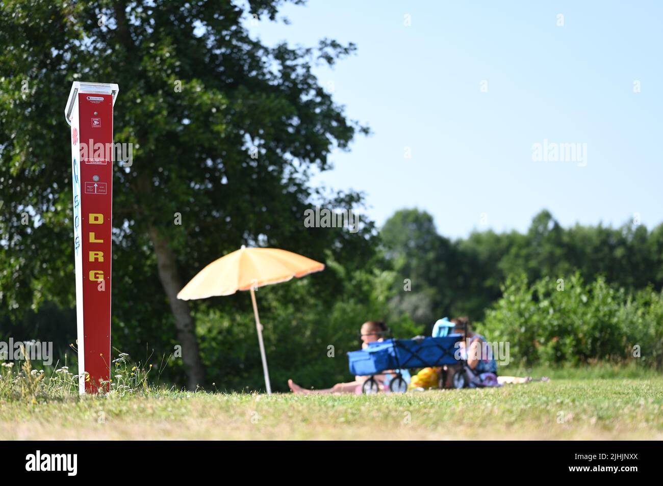 Neermoor, Deutschland. 19.. Juli 2022. Eine Notrufsäule am Badesee. Im Hintergrund sitzen Badegäste auf einer Decke und genießen das Wetter. Quelle: Lars Klemmer/dpa/Alamy Live News Stockfoto
