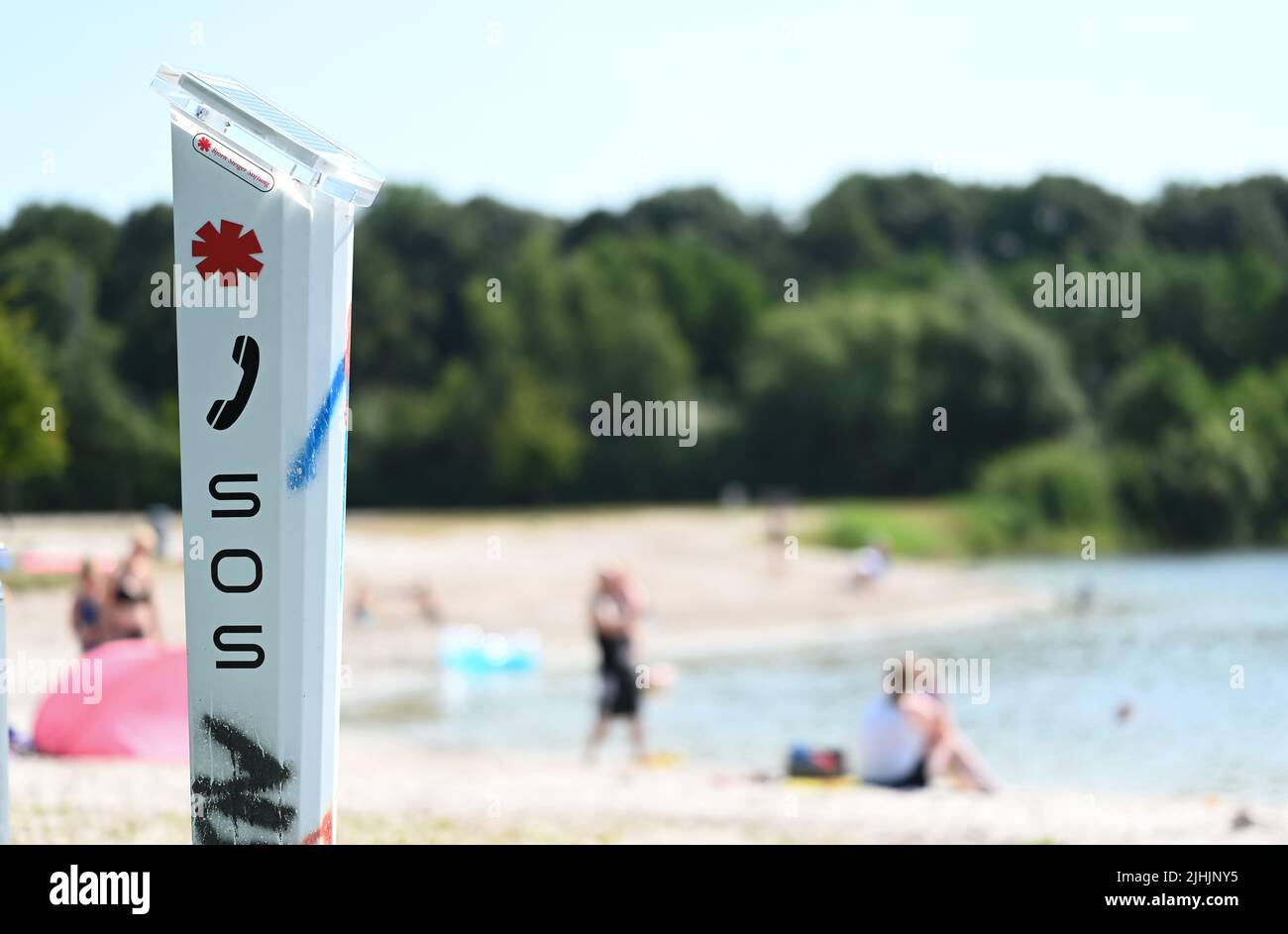 Neermoor, Deutschland. 19.. Juli 2022. An einem unbewachten Badesee in Ostfriesland steht eine DLRG-Notrufsäule. Im Hintergrund sitzen einige Gäste am Strand. Quelle: Lars Klemmer/dpa/Alamy Live News Stockfoto