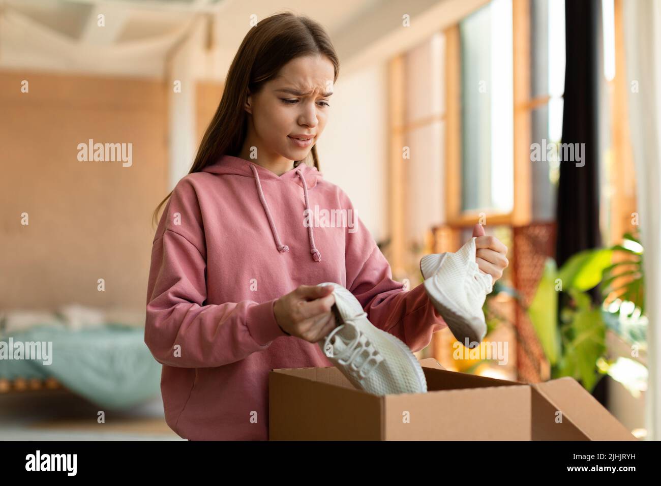 Teen girl unzufrieden mit erhalten Sneaker Schuhe, unzufrieden Kunden Öffnen Box und Blick auf falsch geliefert Artikel Stockfoto