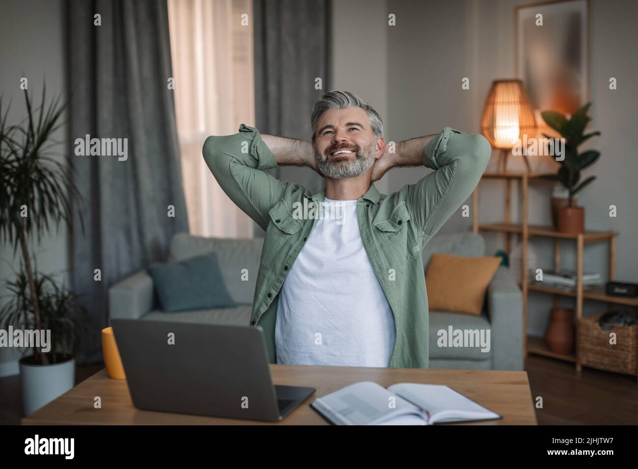 Froher alter europäischer Mann mit Bart Pause am Arbeitsplatz mit Laptop, Ruhe in der Freizeit im Wohnzimmer Stockfoto