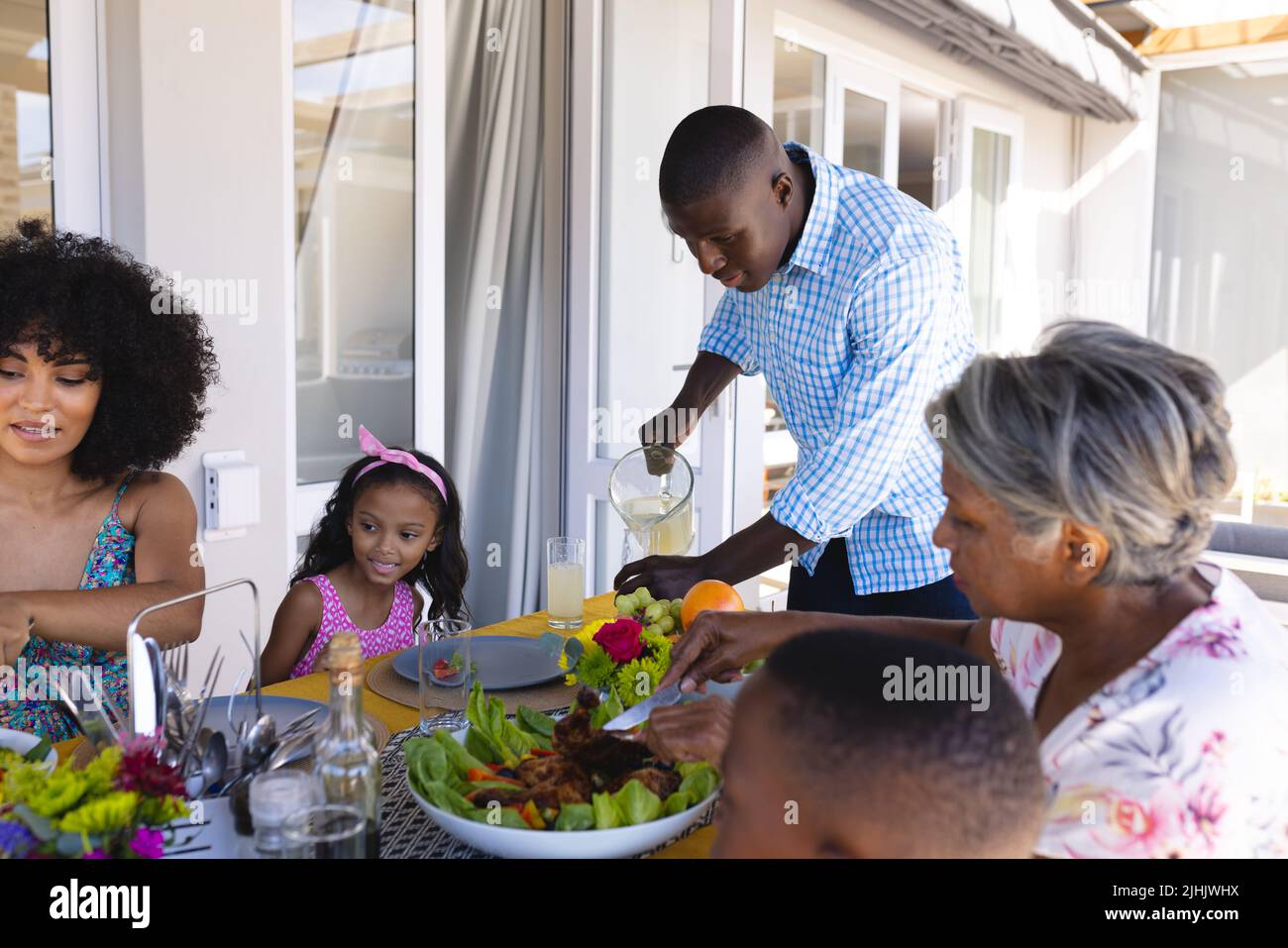 afroamerikanischer Mann, der einer multirassischen Familie Getränke serviert, während er zu Hause am Esstisch zu Mittag gegessen hat Stockfoto