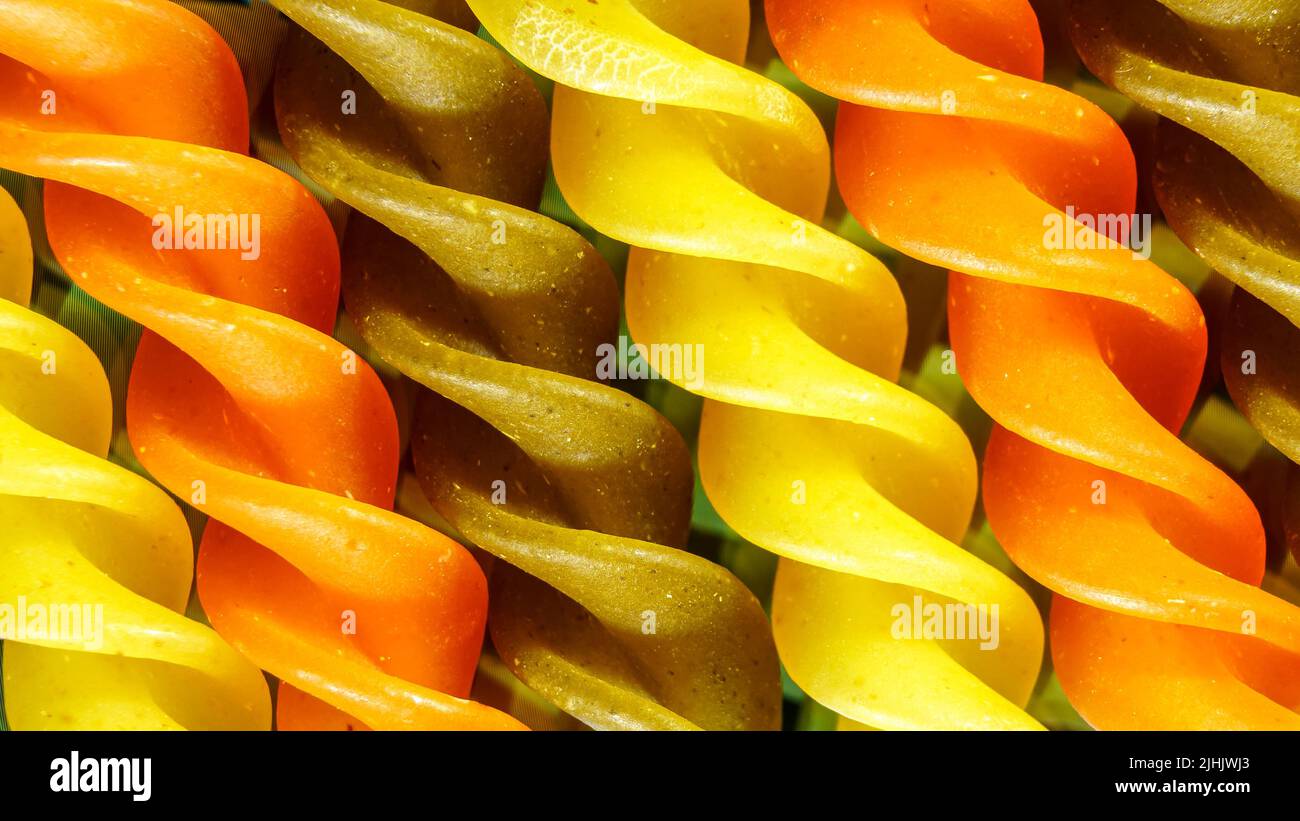 Ungekochte, rohe, dreifarbige Makkaroni-Pasta auf schwarzem Hintergrund. Makroaufnahme von Lebensmitteln. Stockfoto