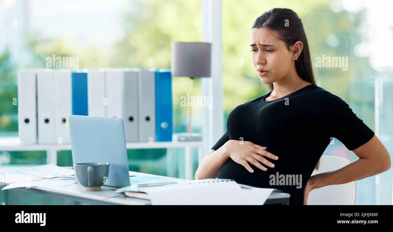 Überfordert und in Schmerzen. Eine Schwangere Geschäftsfrau, die während der Arbeit in einem Büro Schmerzen hat. Stockfoto