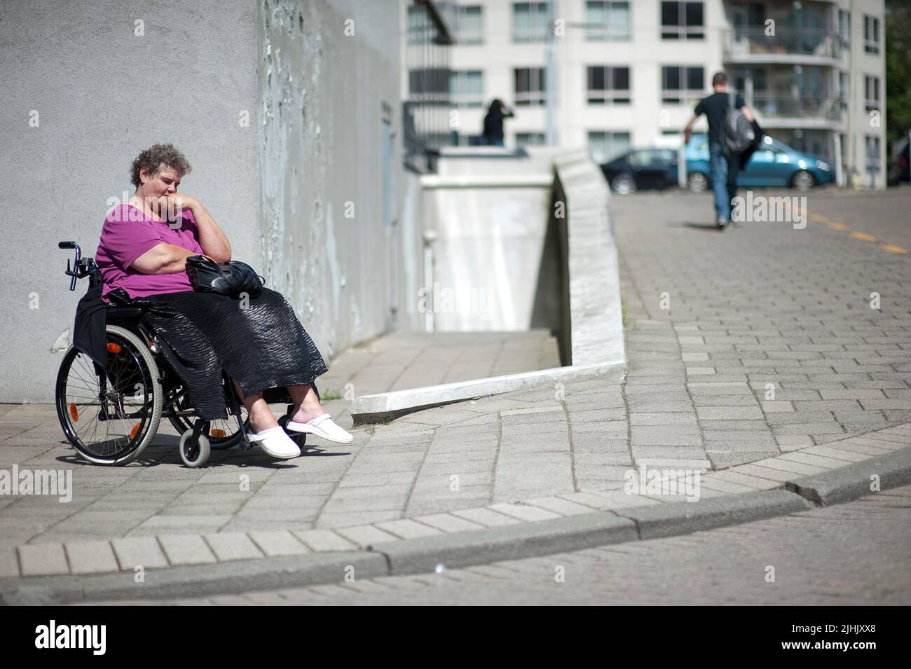 Rotterdam, Niederlande. Eine behinderte Frau im Rollstuhl sitzt an einem warmen Frühlingstag bei einem sonnigen Sport auf dem Bürgersteig. Stockfoto