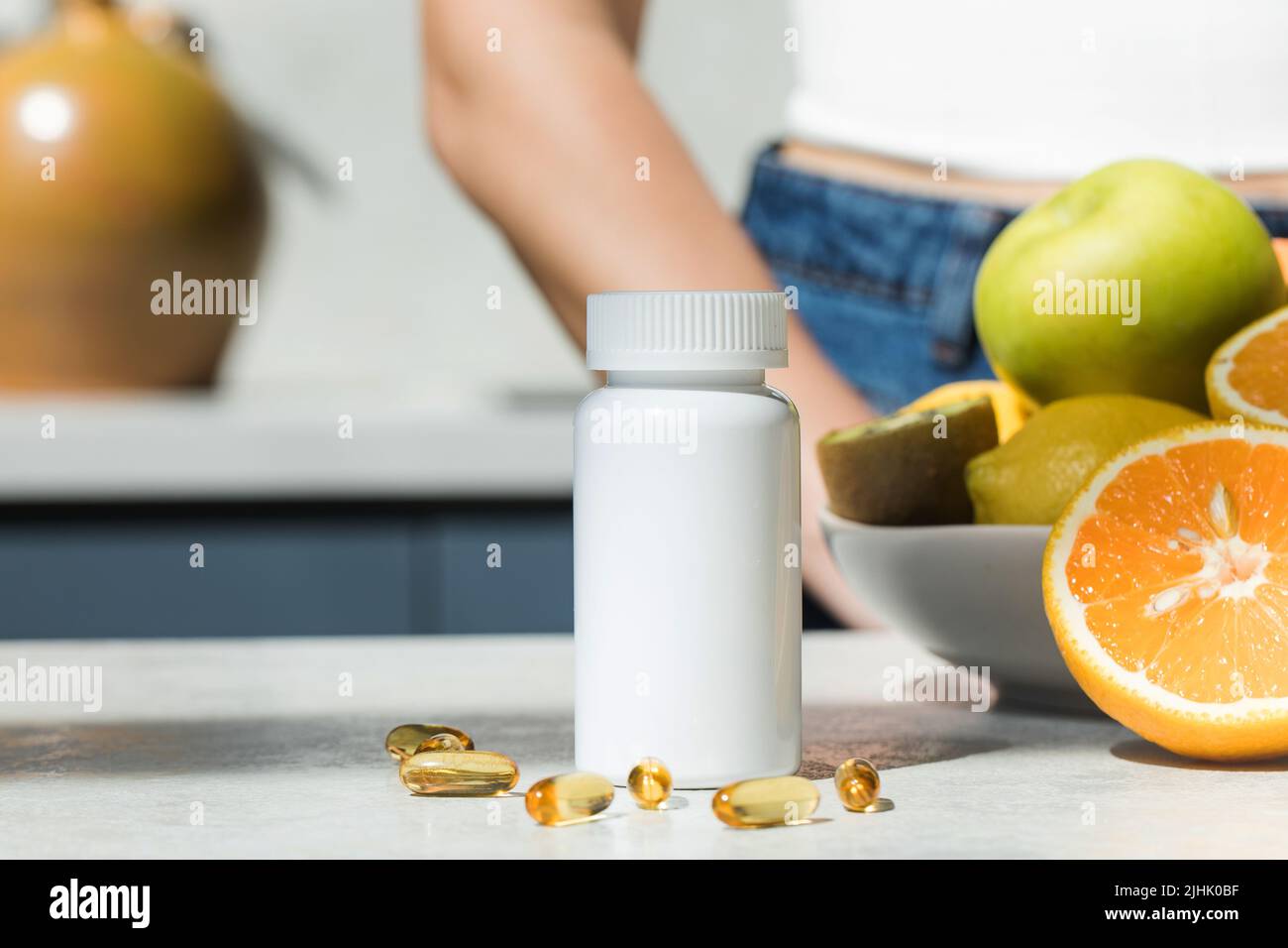 Mockup eines weißen Plastikglases mit Vitamin D- oder Fischölkapseln auf dem Küchentisch. Nahrungsergänzungsmittel. Stockfoto