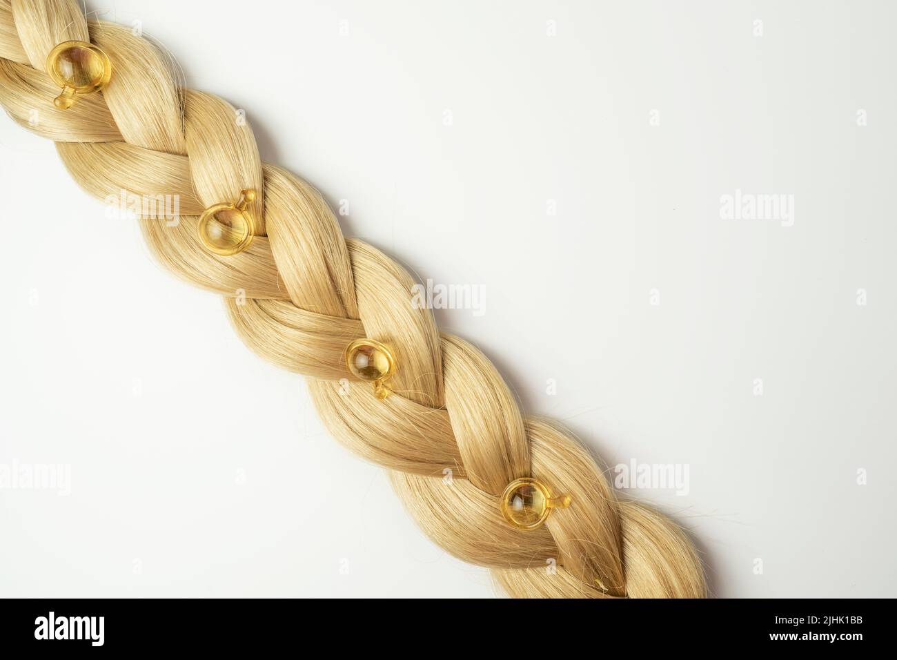 Ein natürliches ätherisches Öl oder Serum für die Haarpflege in goldenen Kapseln, die auf einem Strang blondes Haar liegen. Haarpflege und Glättung Konzept Stockfoto