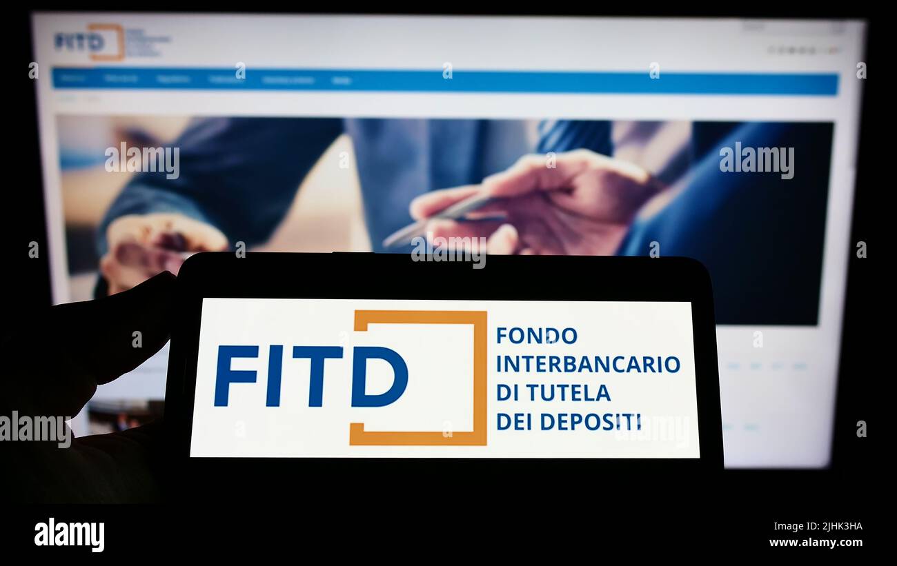 Person mit Mobiltelefon und Logo von Fondo Interbancario di Tutela dei Depositi (FITD) auf dem Bildschirm vor der Webseite. Konzentrieren Sie sich auf die Telefonanzeige. Stockfoto