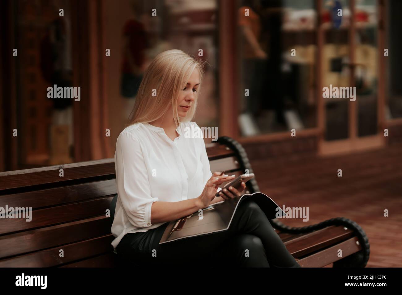 Eine selbstbewusste Geschäftsfrau, die auf der Bank sitzt und über das Projekt arbeitet und mit Kunden telefoniert Stockfoto