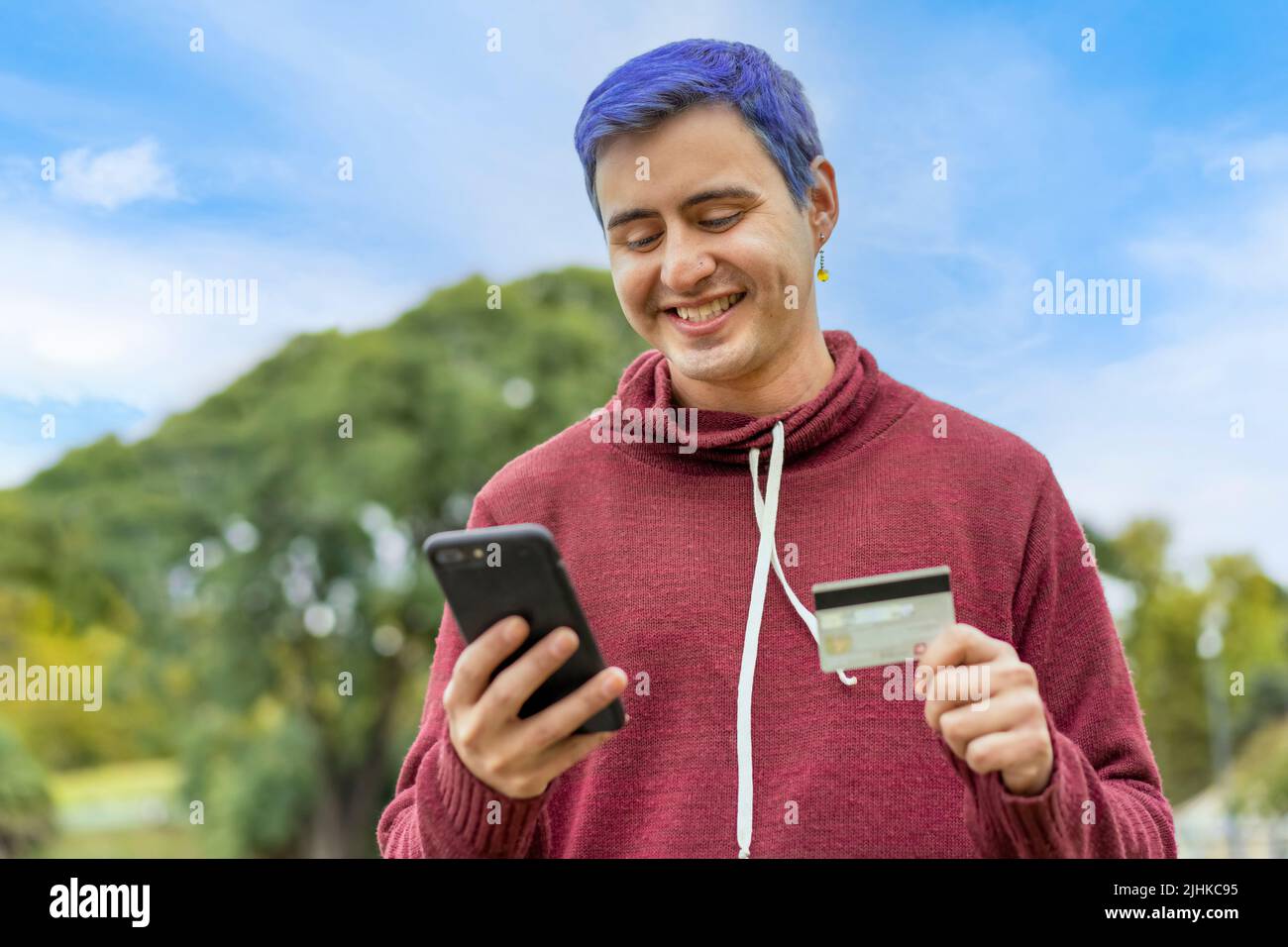 Lateinischer schwuler Mann mit Kreditkarte, um Online-Zahlung auf dem Smartphone zu machen. Gemischter Mann mit Handy zum Online-Shopping. Kerl mit Smartphone zu che Stockfoto