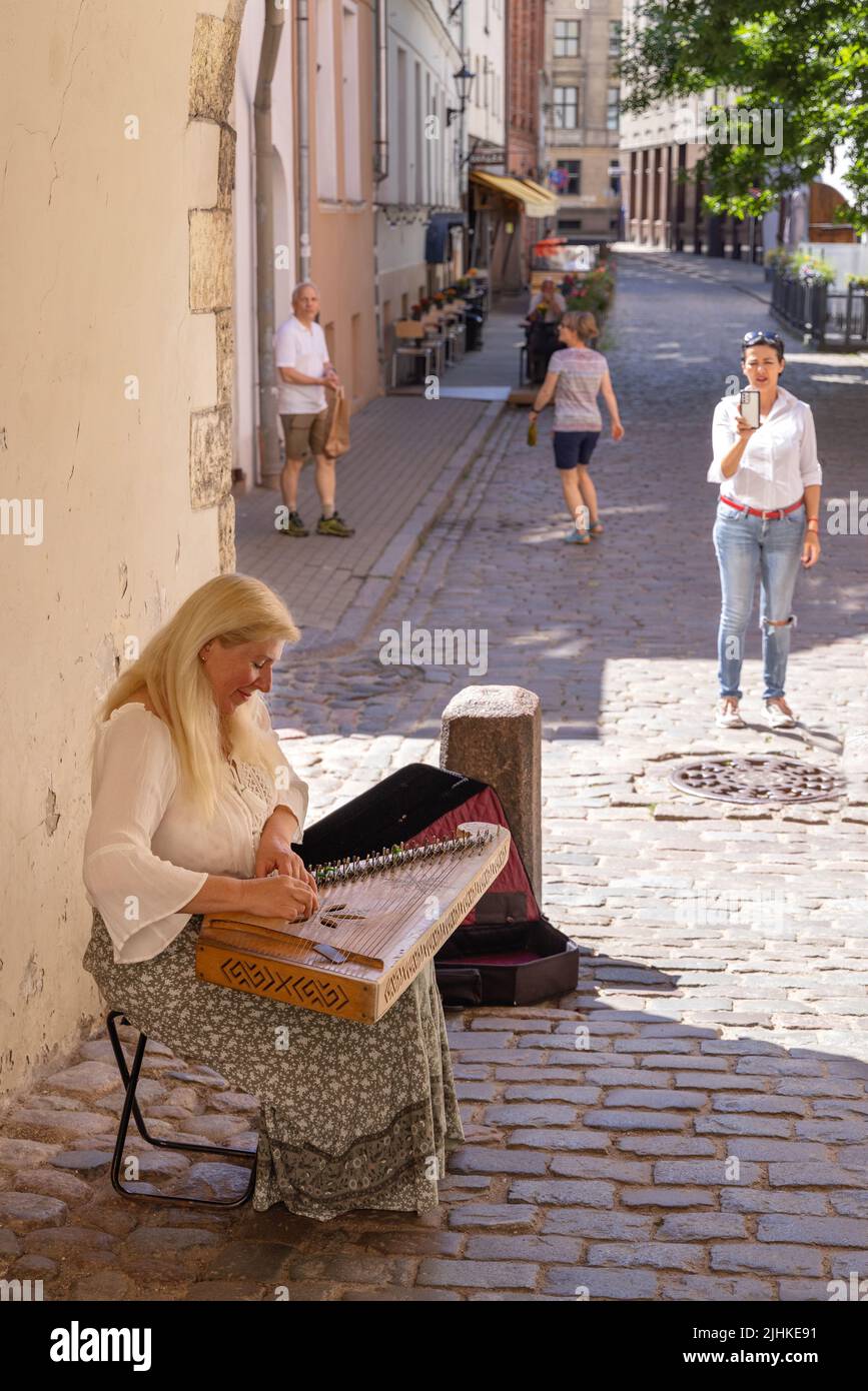 Eine Straßenkünstlerin, die im Sommer auf einer Kopfsteinpflasterstraße Musik spielt, Riga Altstadt, Riga Lettland Europa Stockfoto