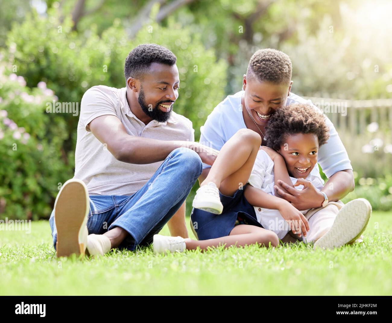 Eine Mutter und ein Vater kitzeln ihren Sohn, während sie sich im Freien entspannen. Stockfoto