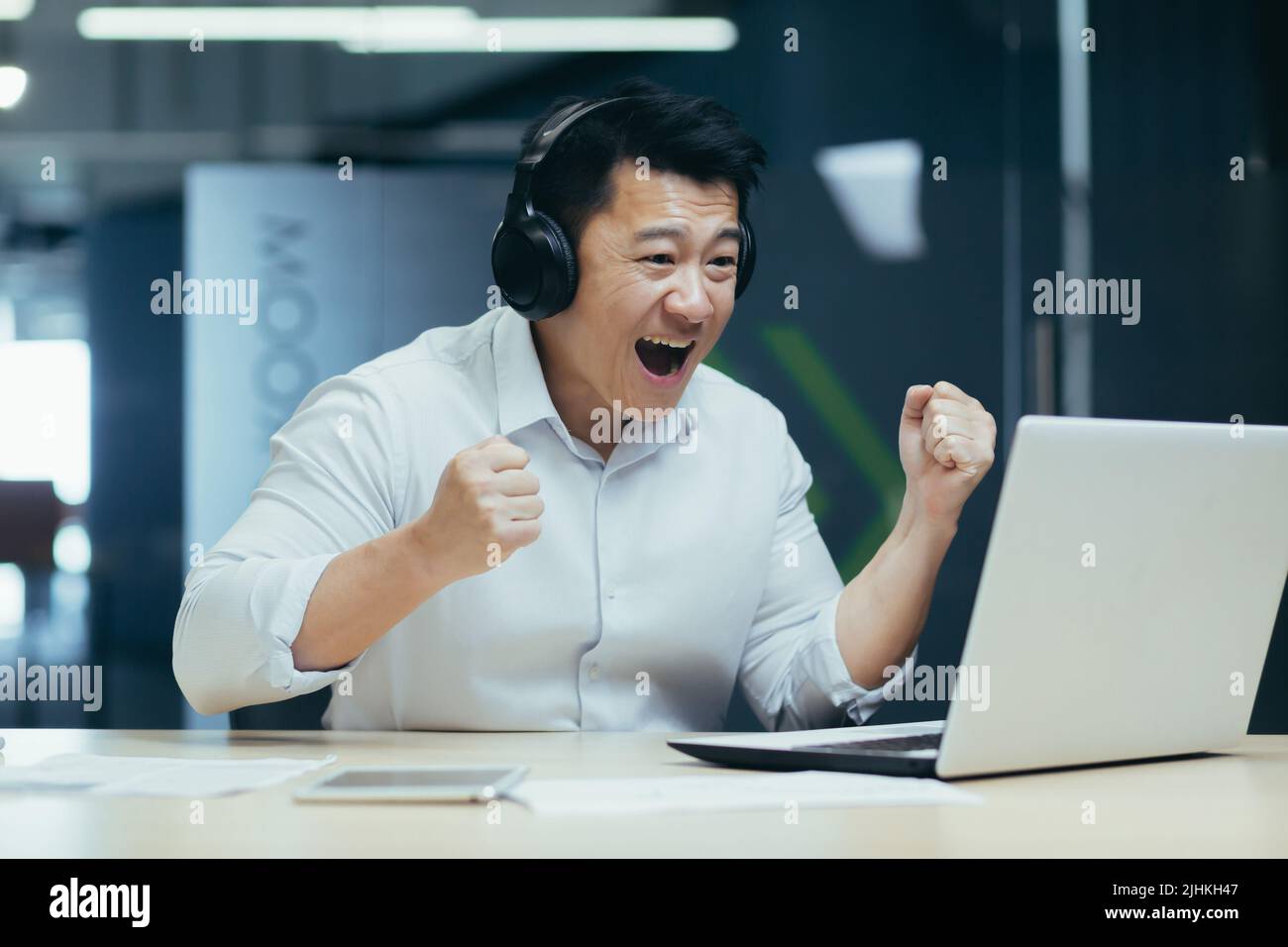 Glücklicher asiatischer Geschäftsmann, der online Sportspiele ansieht, ein Mann im Büro, der fröhlich auf den Laptop-Bildschirm schaut Stockfoto