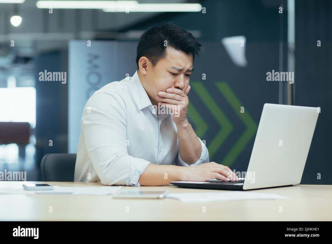 Kranker Mann bei der Arbeit, asiatischer Mann, der durch schlechtes Mittagessen vergiftet wird, Geschäftsmann, der mit einem Laptop im modernen Büro arbeitet Stockfoto