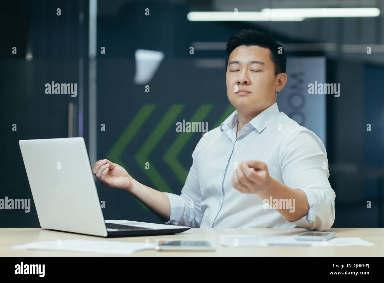 Porträt eines asiatischen Geschäftsmannes, eines Mannes im Büro, der mit einem Laptop arbeitet und am Arbeitsplatz mit geschlossenen Augen meditiert Stockfoto