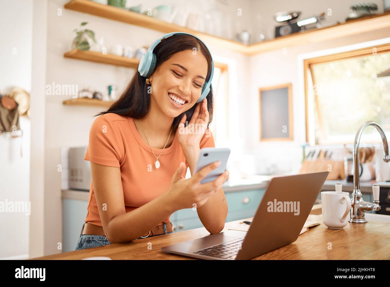 Junge schöne fröhliche gemischte Rennen Geschäftsfrau hält und mit einem Telefon, während Kopfhörer und Musik von zu Hause aus zu hören. Eins Stockfoto