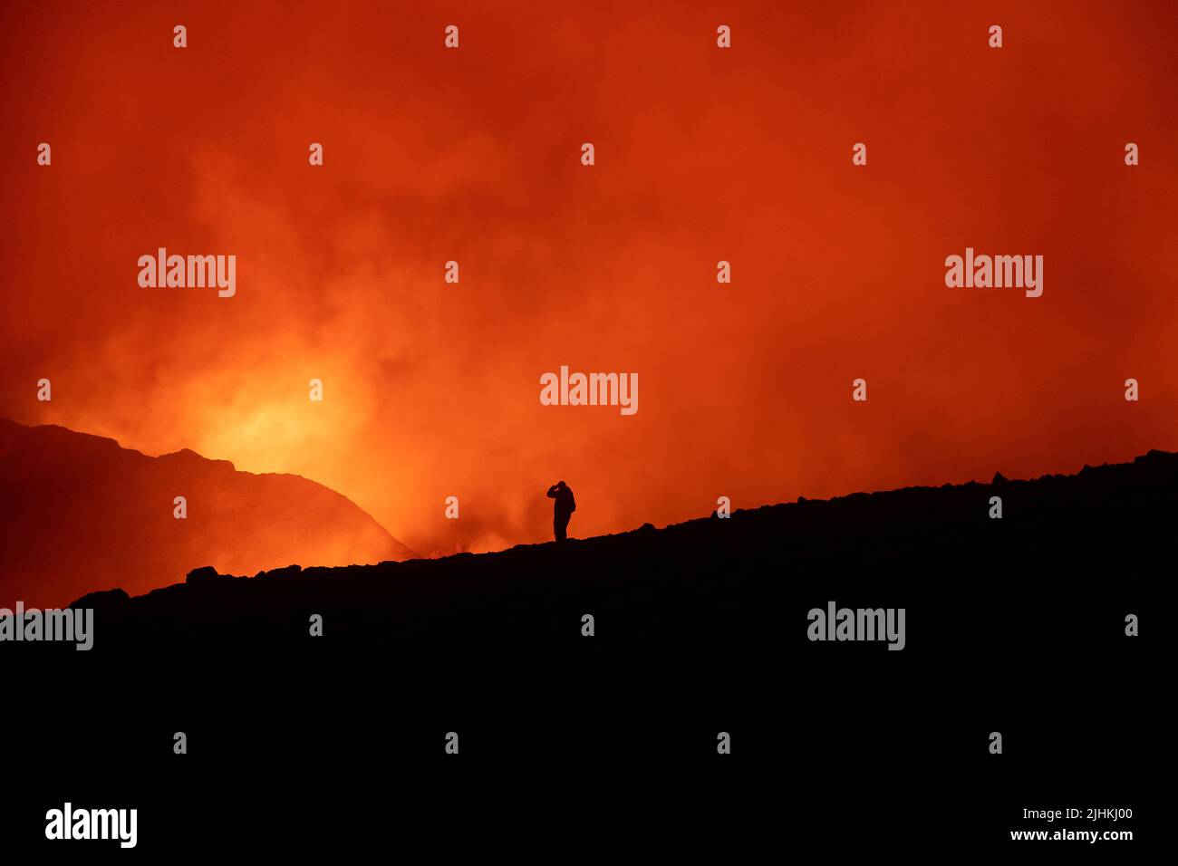 Eine schwarze Silhoutte eines Touristen, der während der Eruption in Island im Jahr 2021 gegen den feuerbeleuchteten Himmel gerichtet ist, blickt die Person auf die Eruption in der Stockfoto