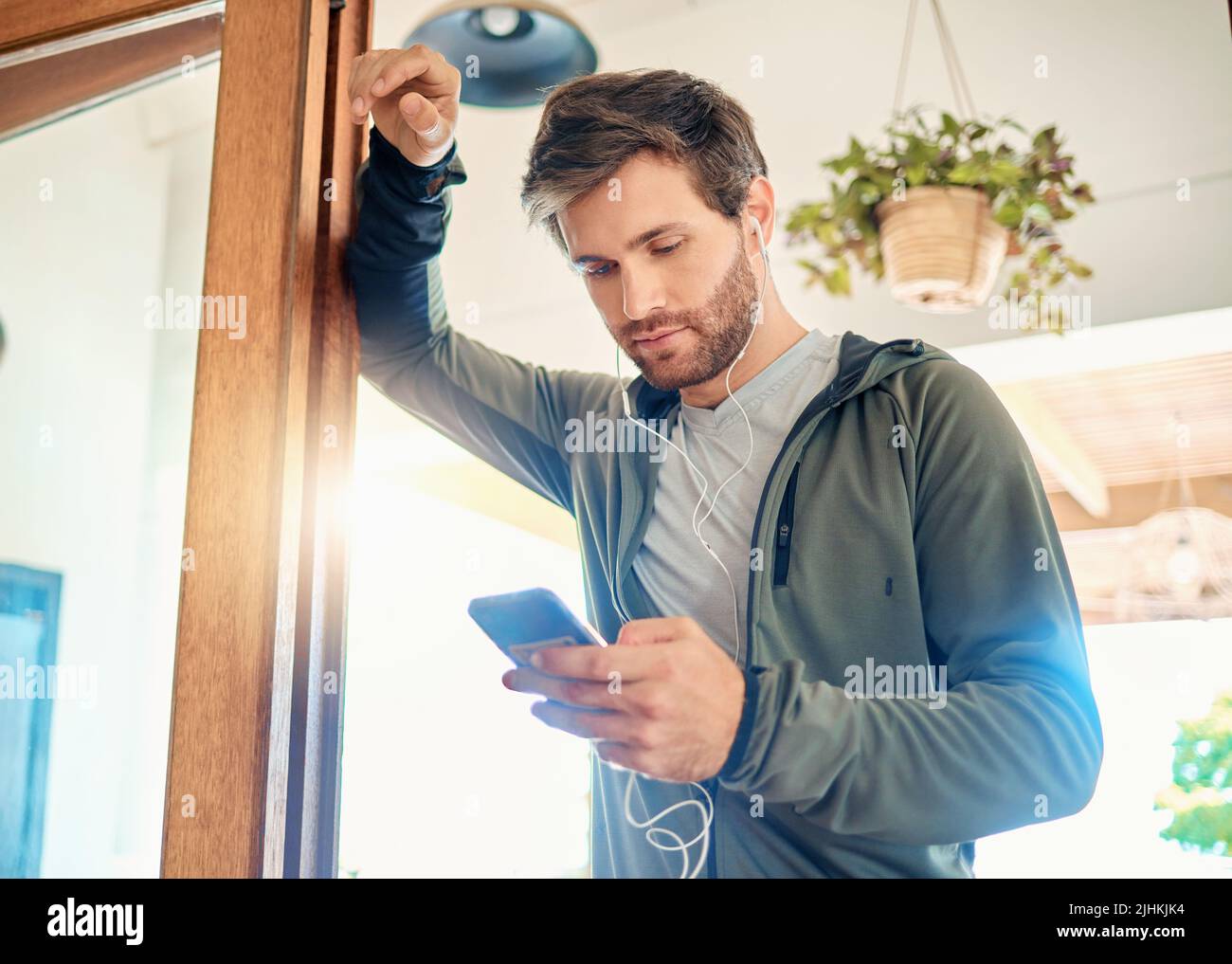 Ein junger Kaukasier hörte Musik mit Kopfhörern von einem Handy, während er eine Pause von der Übung zu Hause nahm. Guy SMS und Verwendung Stockfoto