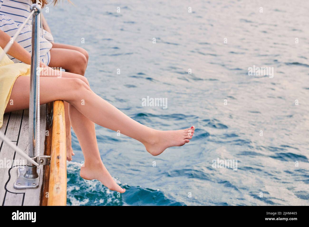 Beine von zwei Frauen, die während der Kreuzfahrt an der Seite eines Bootes hängen. Zwei Freunde im Urlaub zusammen mit Beinen, die über der Seite des Bootes hängen Stockfoto