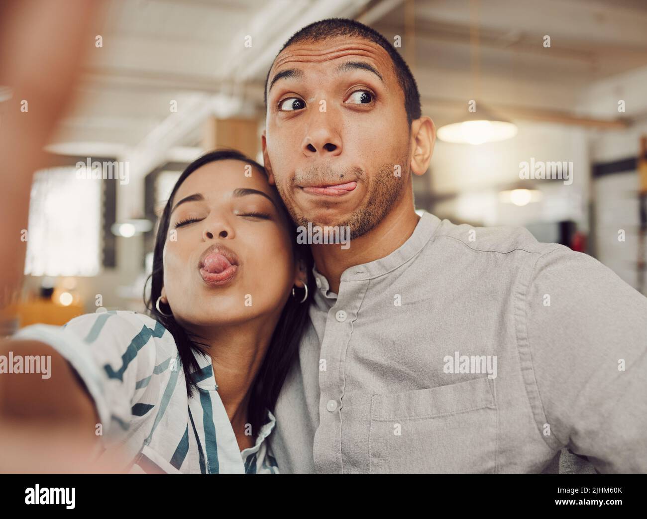 Nahaufnahme einer lustigen jungen Frau, die ein Mobiltelefon hält, während sie ein Selfie mit ihrem Freund macht und in einem Café Gesichter macht. Liebevolle gemischte Rasse Paar sein Stockfoto