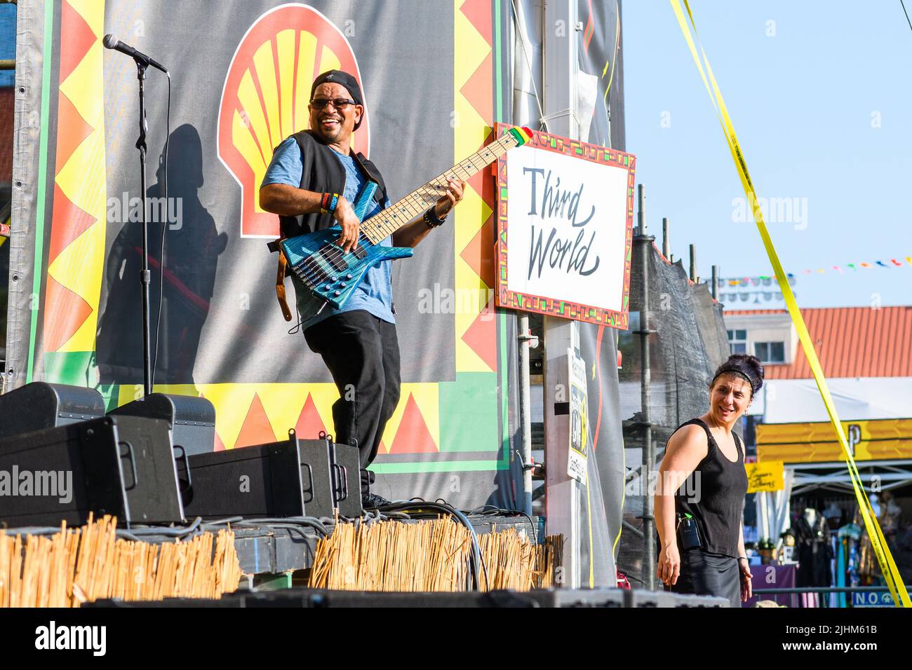 NEW ORLEANS, LA, USA - 29. April 2022: Richard Daley spielt Bass vor dem Schild der Dritten Welt, wobei eine Frau dabeisteht, um die Gebärdensprache zu interpretieren Stockfoto