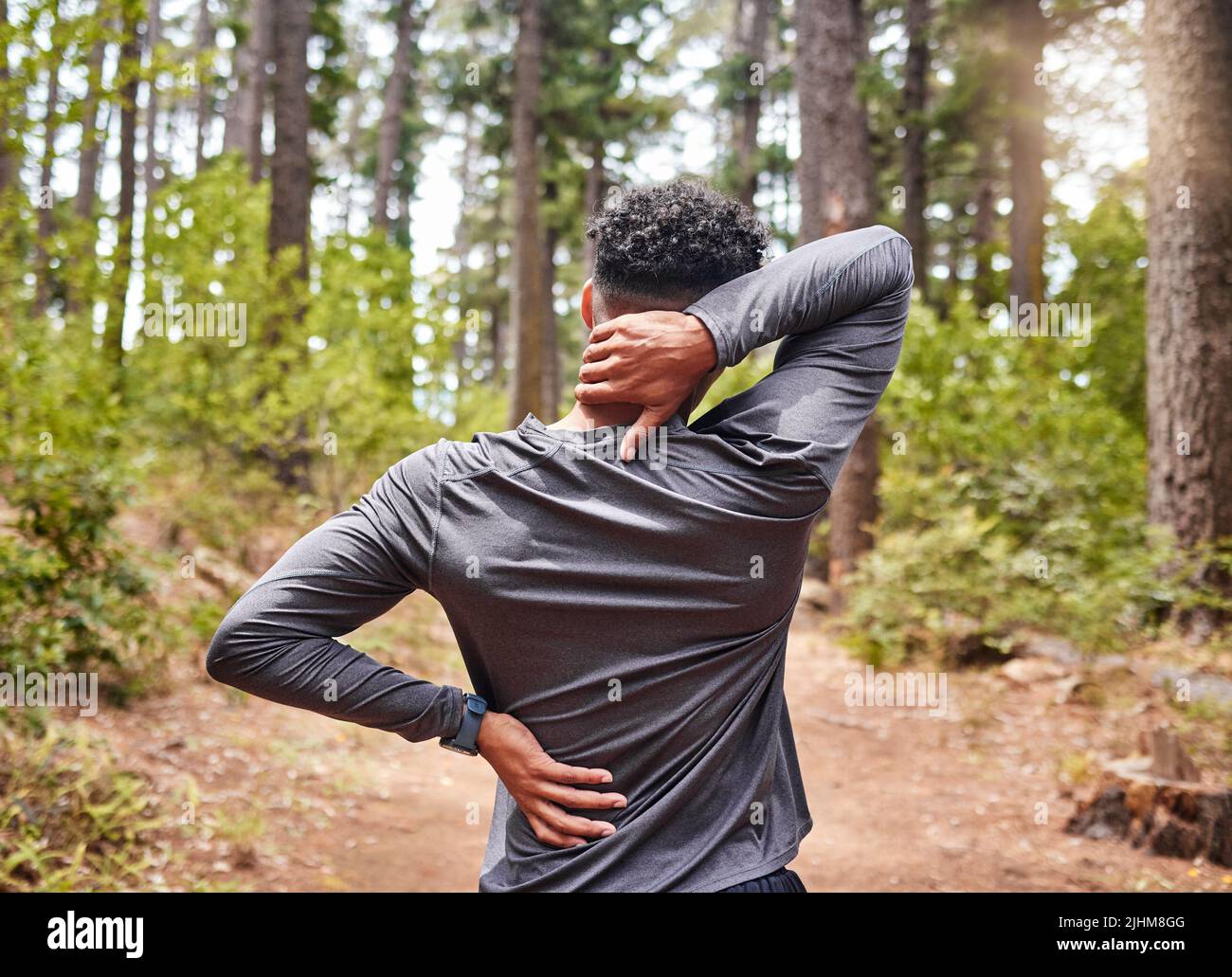 Nicht erkennbare Mischrasse hispanic männlich Stretching vor einem Lauf, während einige Rücken-und Nackenschmerzen in einem Wald. Übung ist gut für Ihre Stockfoto