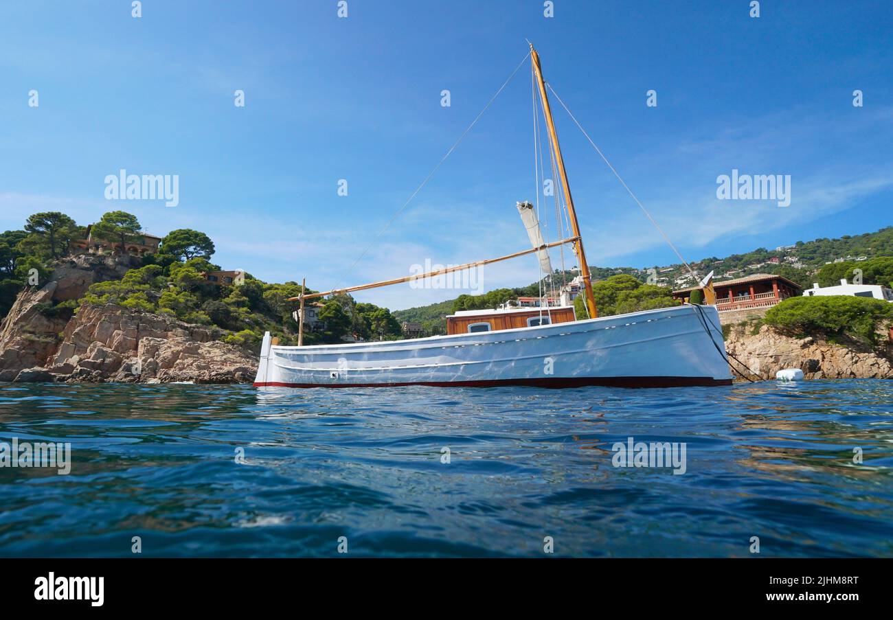 Typisches mediterranes Boot, das in der Nähe der felsigen Küste mit Häusern von der Meeresoberfläche aus gesehen, Spanien, Costa Brava, Begur, Katalonien festgemacht ist Stockfoto