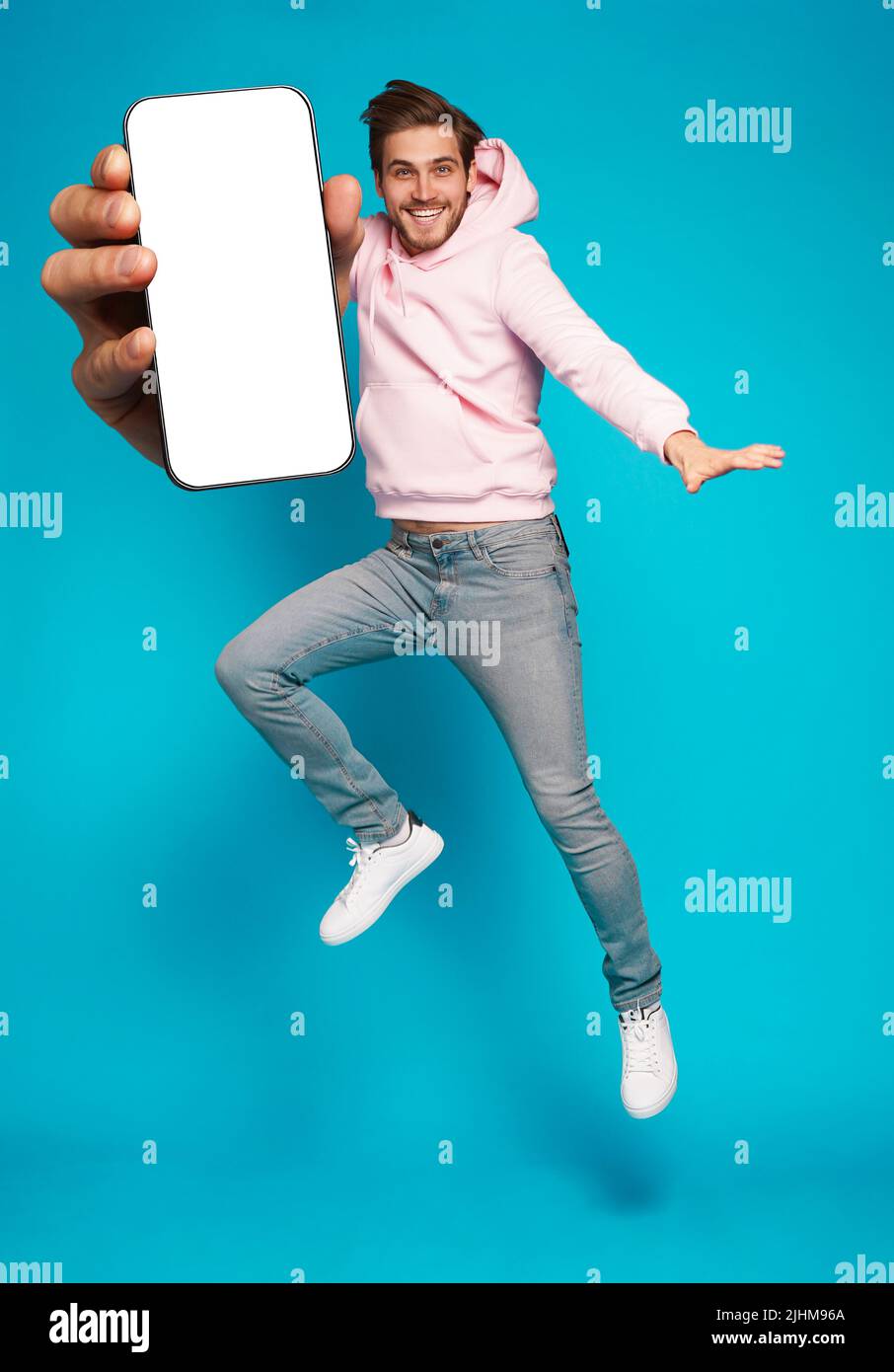 Werbung Für Mobile Apps. Schöner Aufgeregt Mann Zeigt Auf Leeren Smartphone-Bildschirm Posiert Über Hellblauen Studio Hintergrund, Lächelnd Zu Kamera Stockfoto