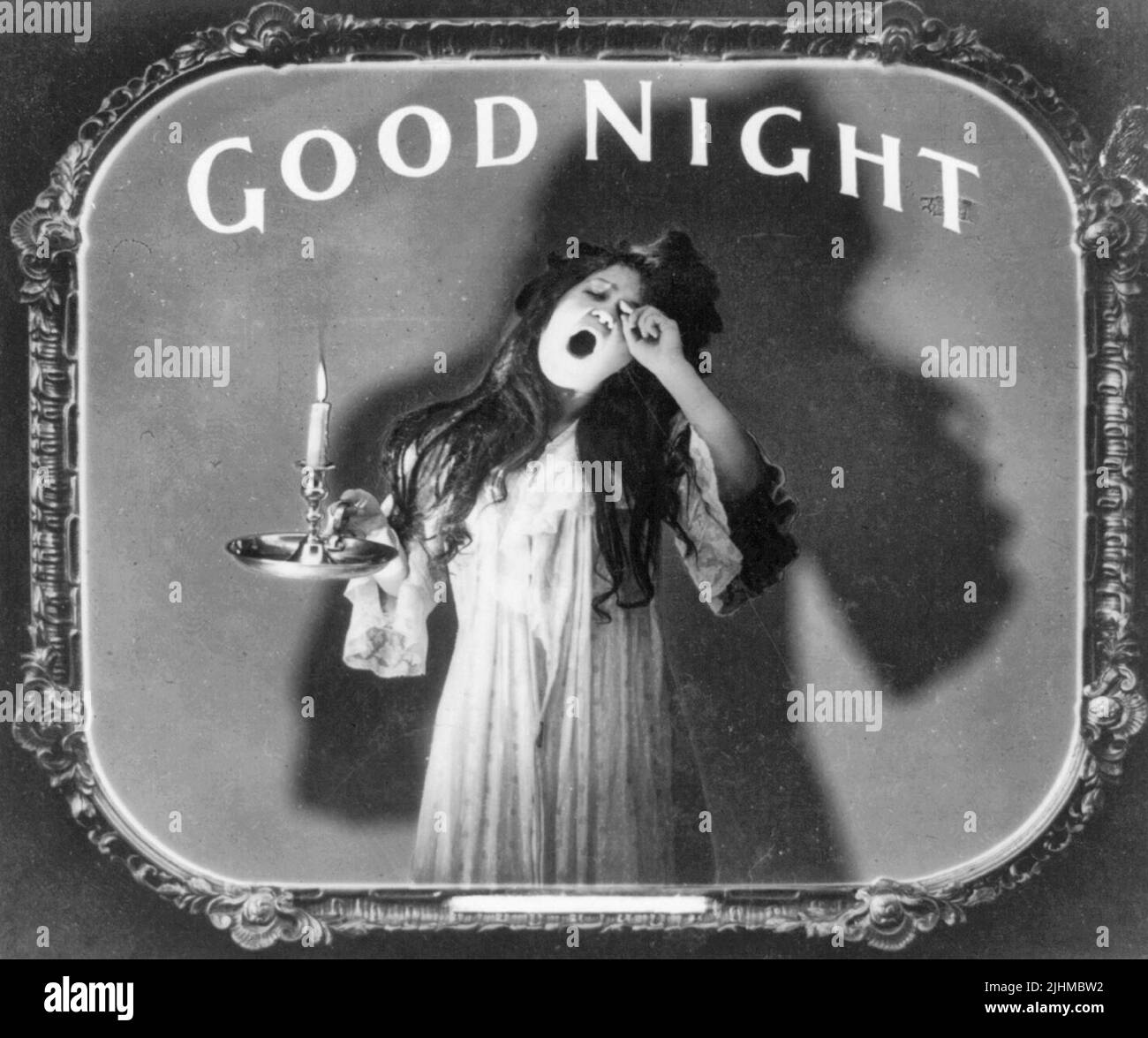 Gute Nacht - Foto zeigt eine Frau, die in ihrer Nachtkleidung gähnt, während sie eine brennende Kerze hält. Positiver Papierdruck von Laternenfolie, der in Filmtheatern als Ankündigung verwendet wird. Stockfoto