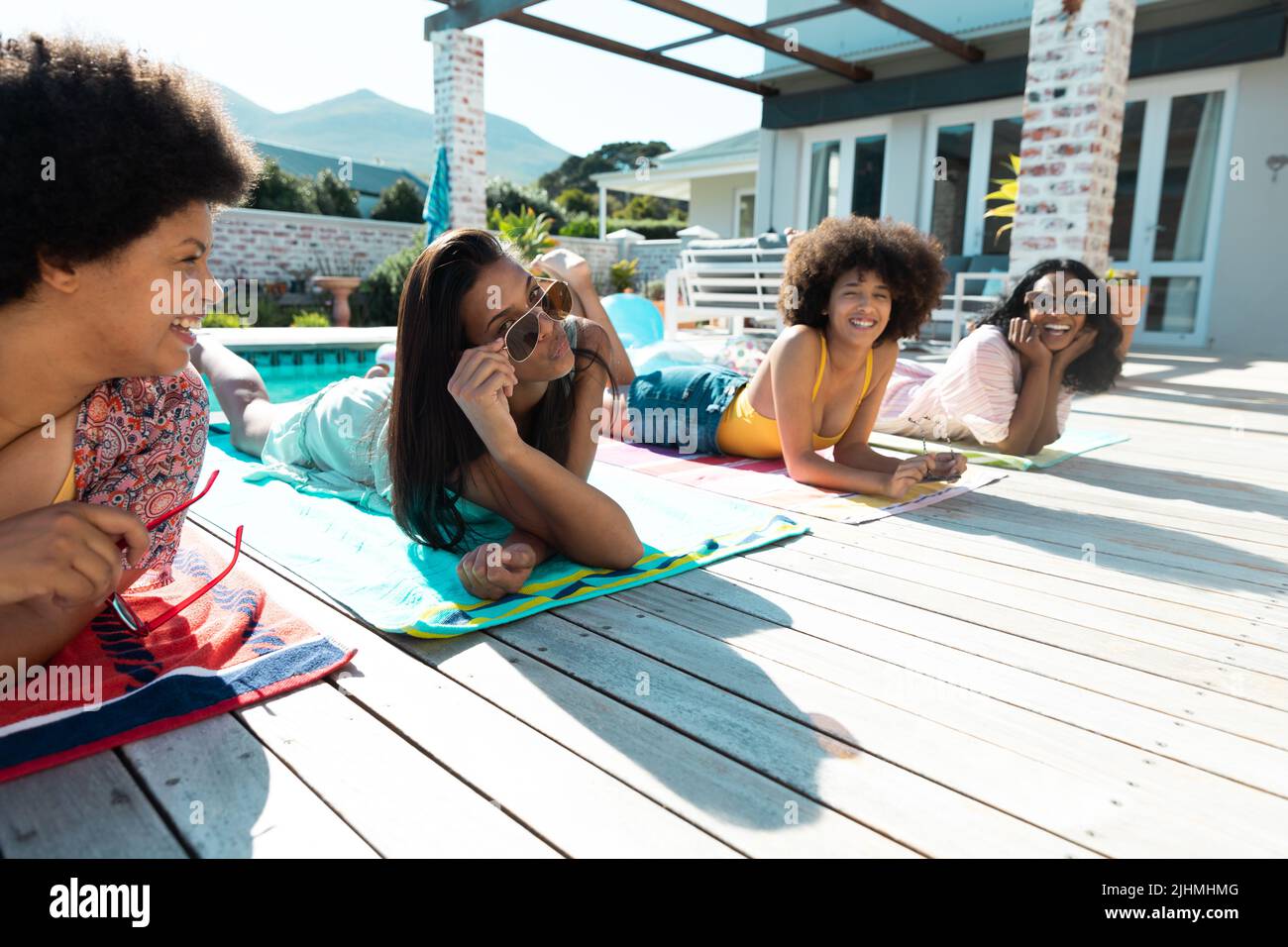 Unbeschwerte Biracial junge Freundinnen liegen auf Handtüchern, während sie am Pool im Sommer hängen Stockfoto