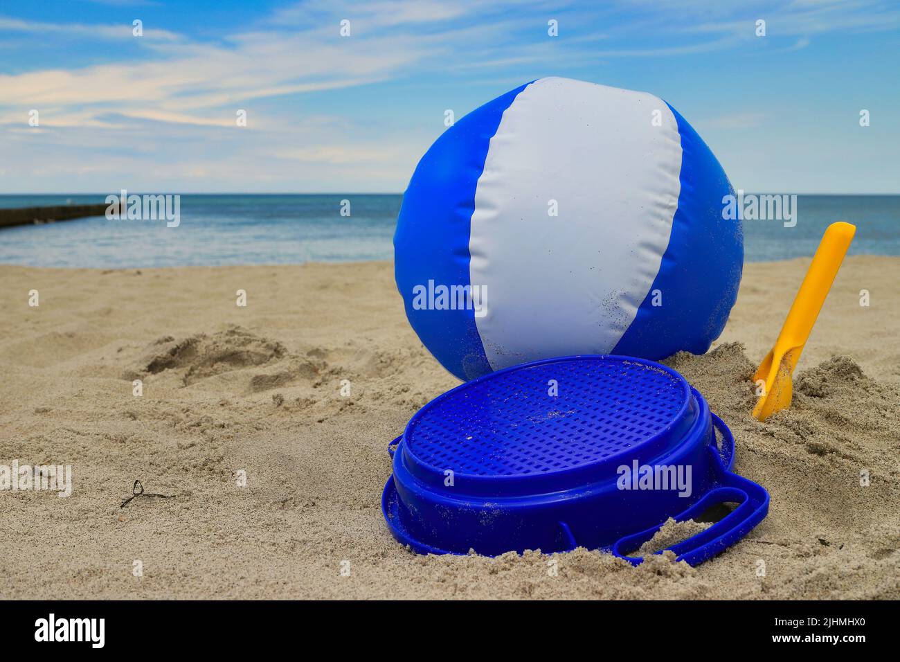 Ball und Spielzeug am sonnigen Sommerstrand mit Meer und Himmel im Hintergrund Stockfoto