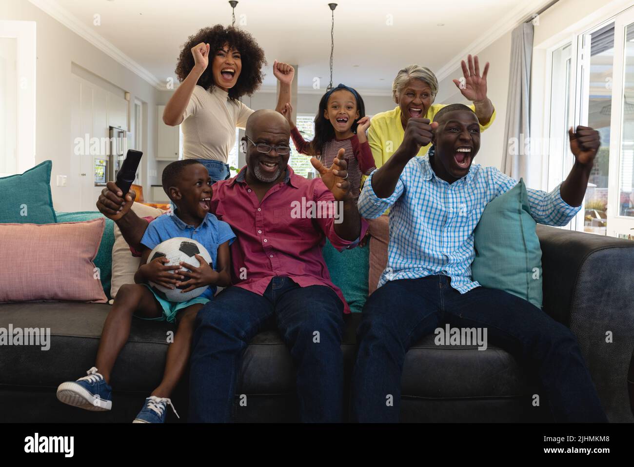 Fröhliche, multirassische Familie, die viele Generationen lang vor Freude schreit, während sie sich zu Hause ein Fußballspiel ansieht Stockfoto