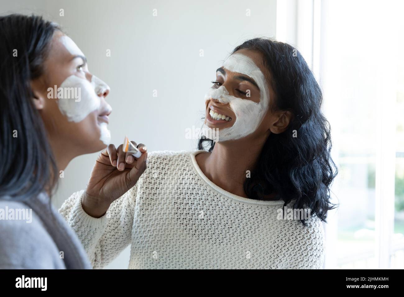 Biracial lächelndes junges Weibchen, das Gesichtscreme auf das Gesicht eines tausendjährigen Freundes zu Hause anwendet Stockfoto