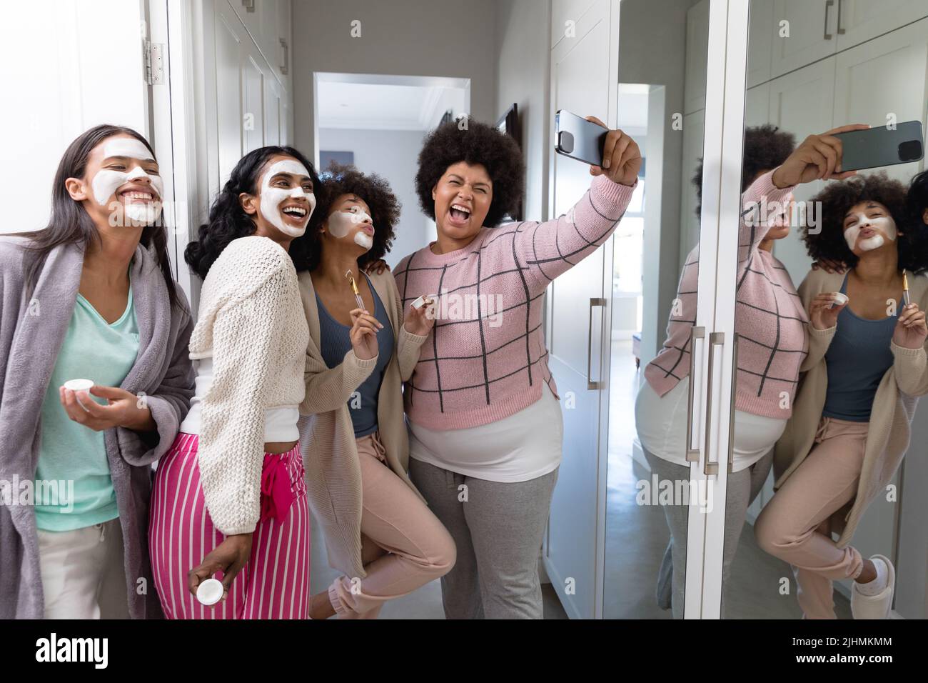 Fröhliche Birazialfrau, die schreit und Selfie mit Freundinnen mit Schönheitscreme auf Gesichtern nimmt Stockfoto