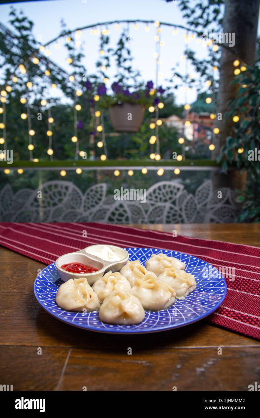 manti und Sauce auf einem blauen Teller auf einem Burgund Hintergrund Stockfoto