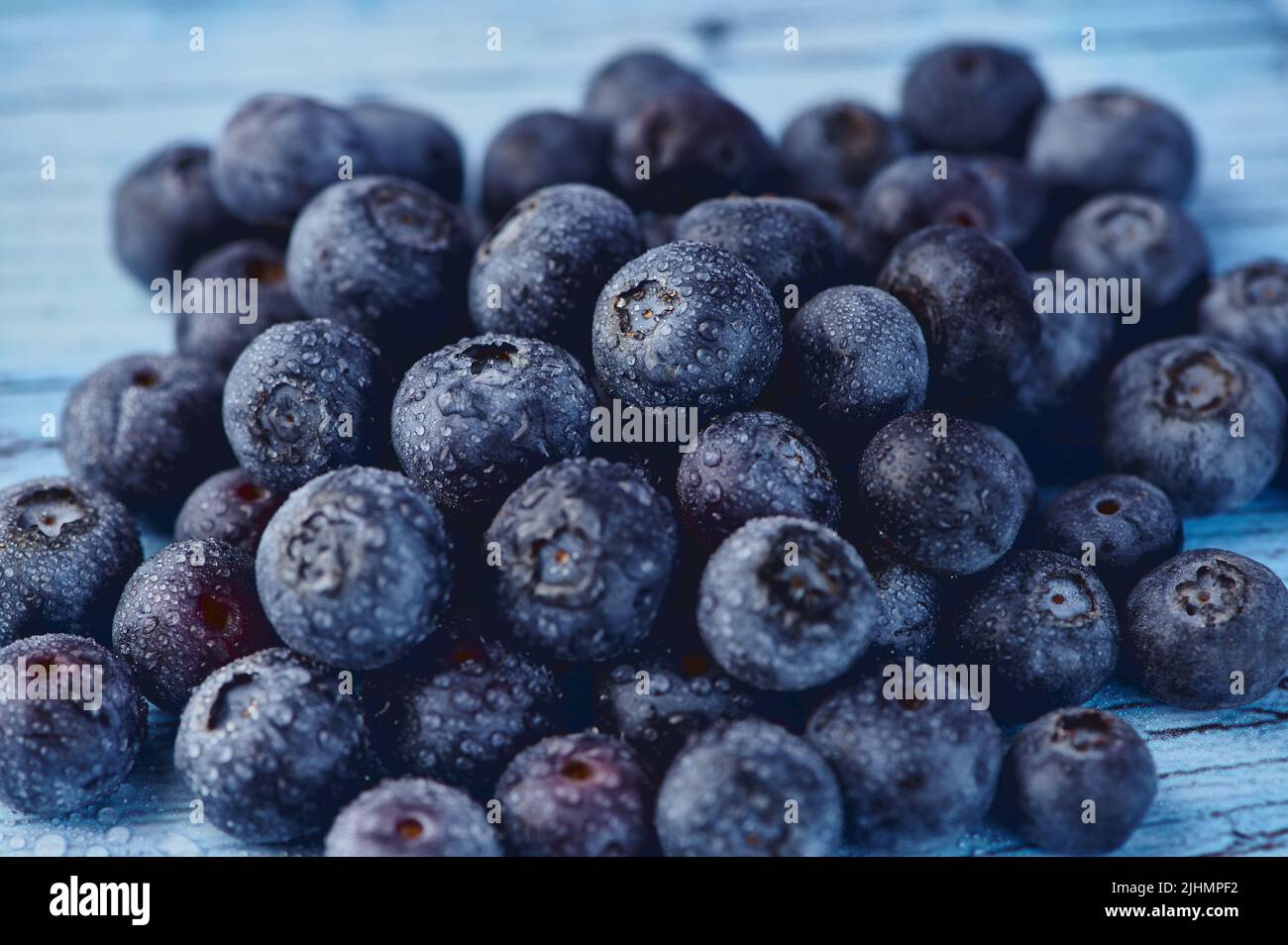 Haufen frischer roher Heidelbeeren mit Wassertropfen auf blauem Hintergrund Stockfoto